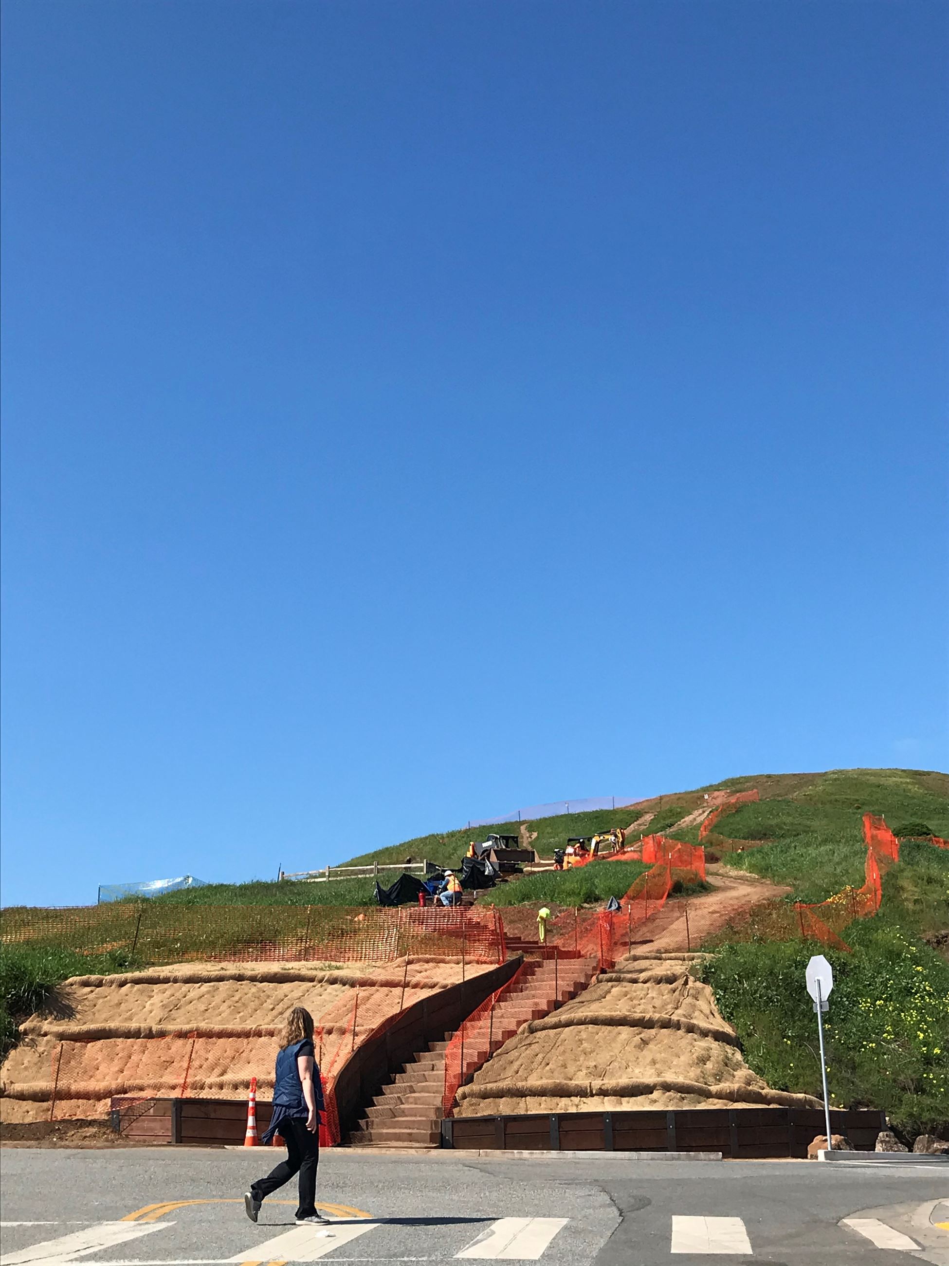 View of Box Steps Up Bernal Hill in construction with orange construction fencing, crosswalk (person