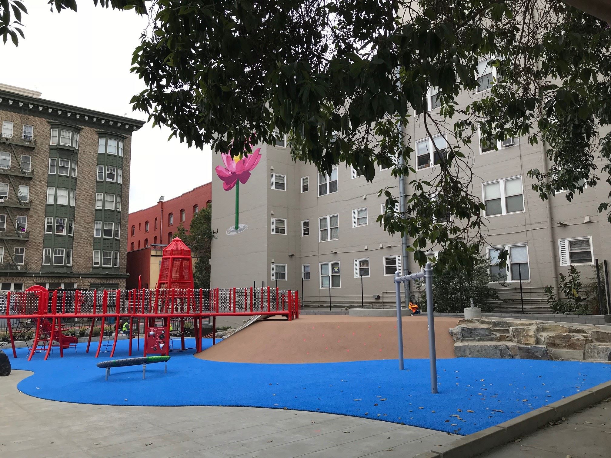 View of the new red play structure with gangway, turret, slide, rope net climbers in the center of t