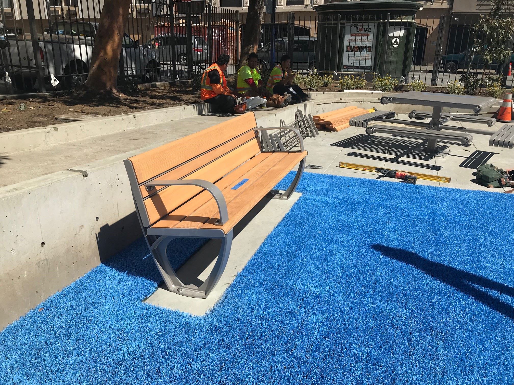 In the center of the photo is a brown and metal standard park bench and a metal picnic table style b
