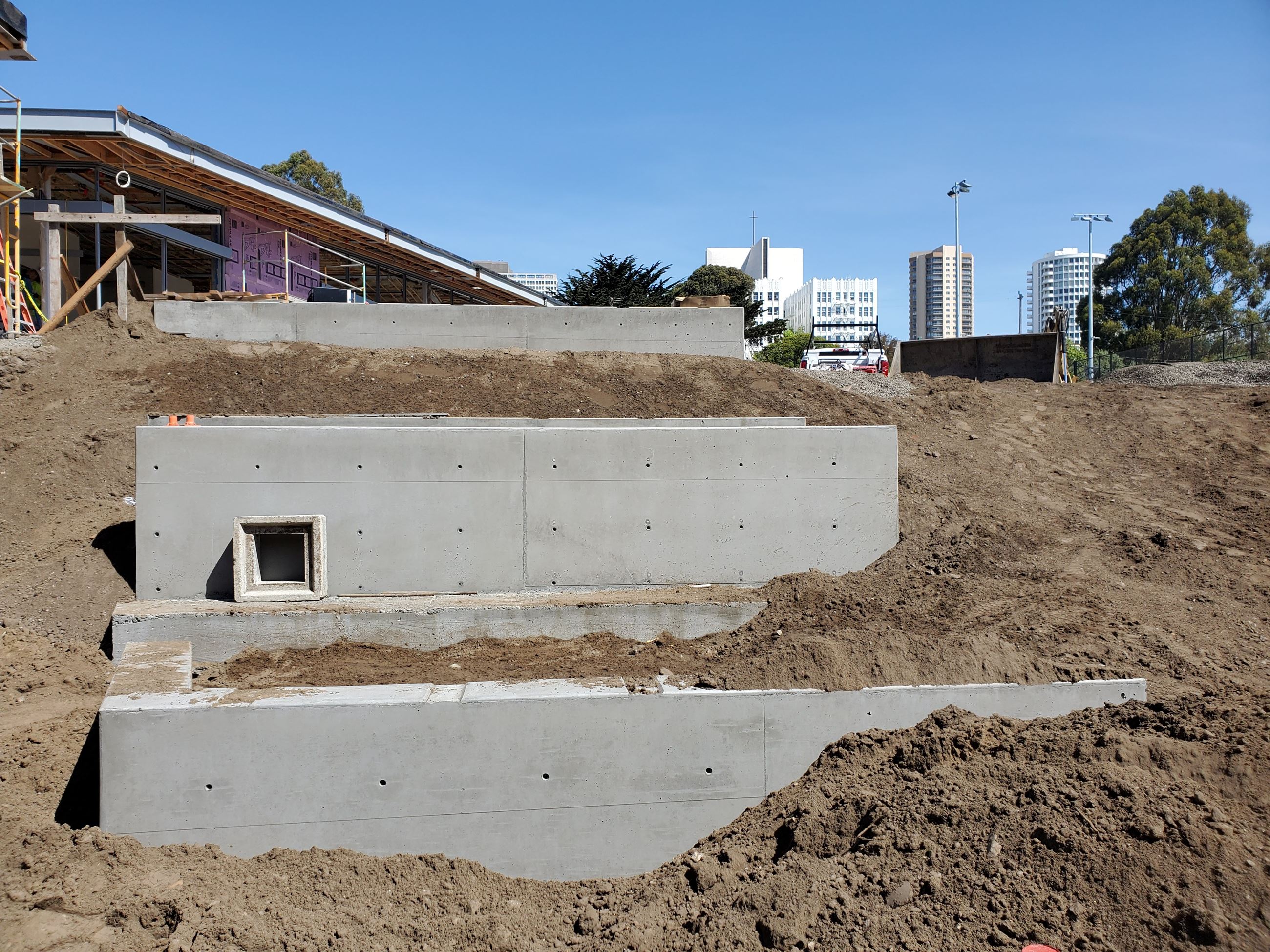 Margaret Hayward Cement Planters with soil material surrounding them on a slope in the foreground an