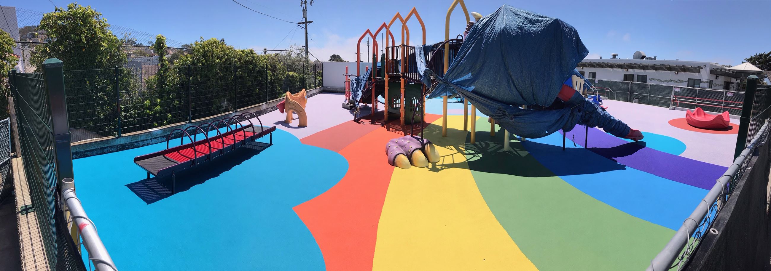 Image is of the West Portal Playground. The ground is covered in a poured in place rubber surfacing 