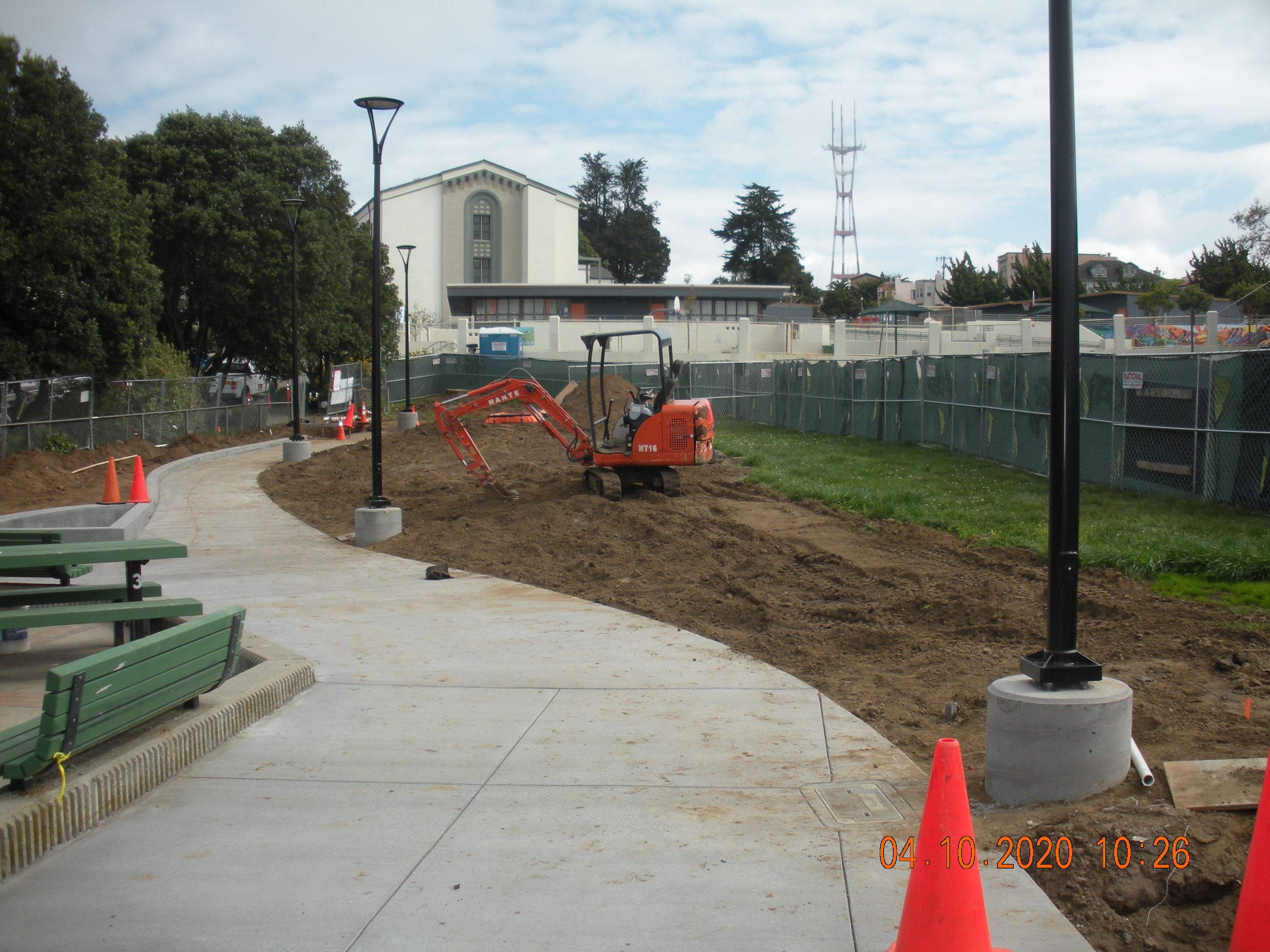 Image shows the concrete pathway and new light poles. The pathway is flanked by several orange cones