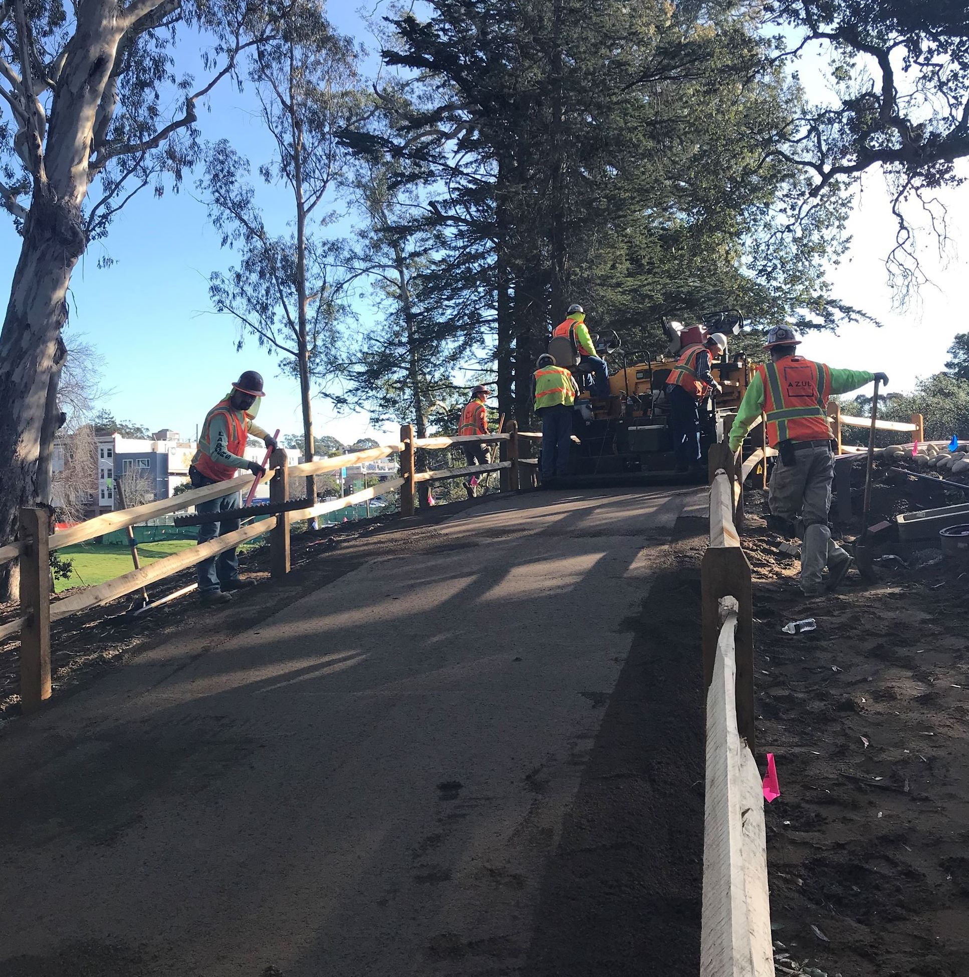Image shows six construction workers wearing bright neon yellow and orange vests finishing work on a