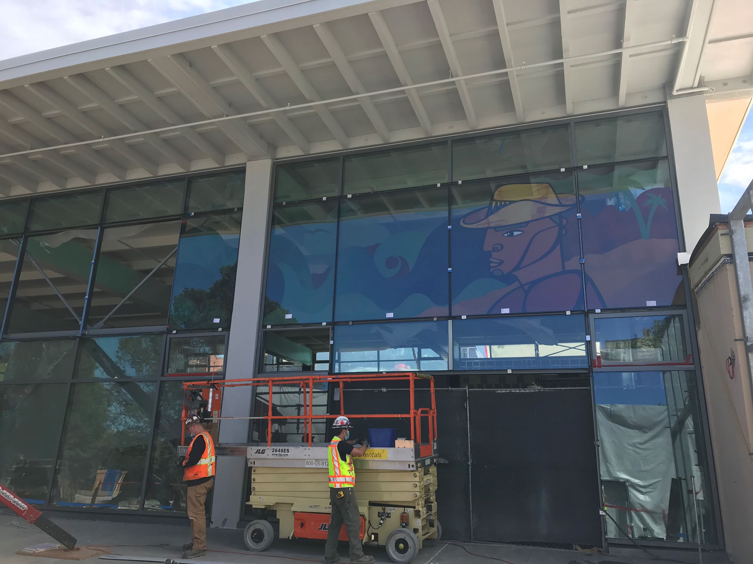 Image is of one construction worker wearing an orange safety vest over a black long sleeve shirt, Kh
