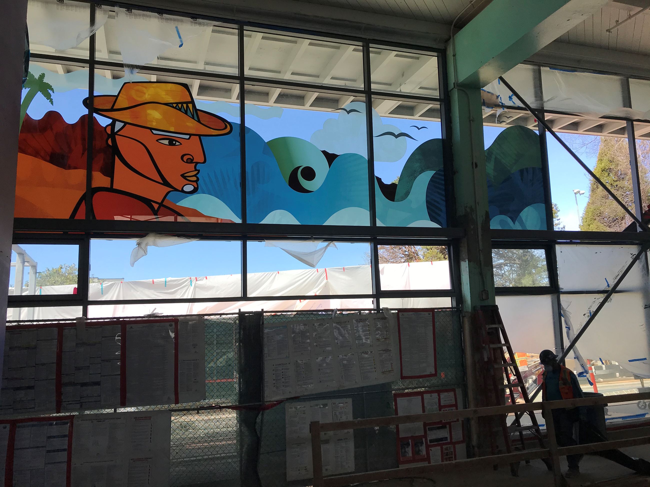 Image shows a construction worker in the shadows of the building standing in front of the glass wind