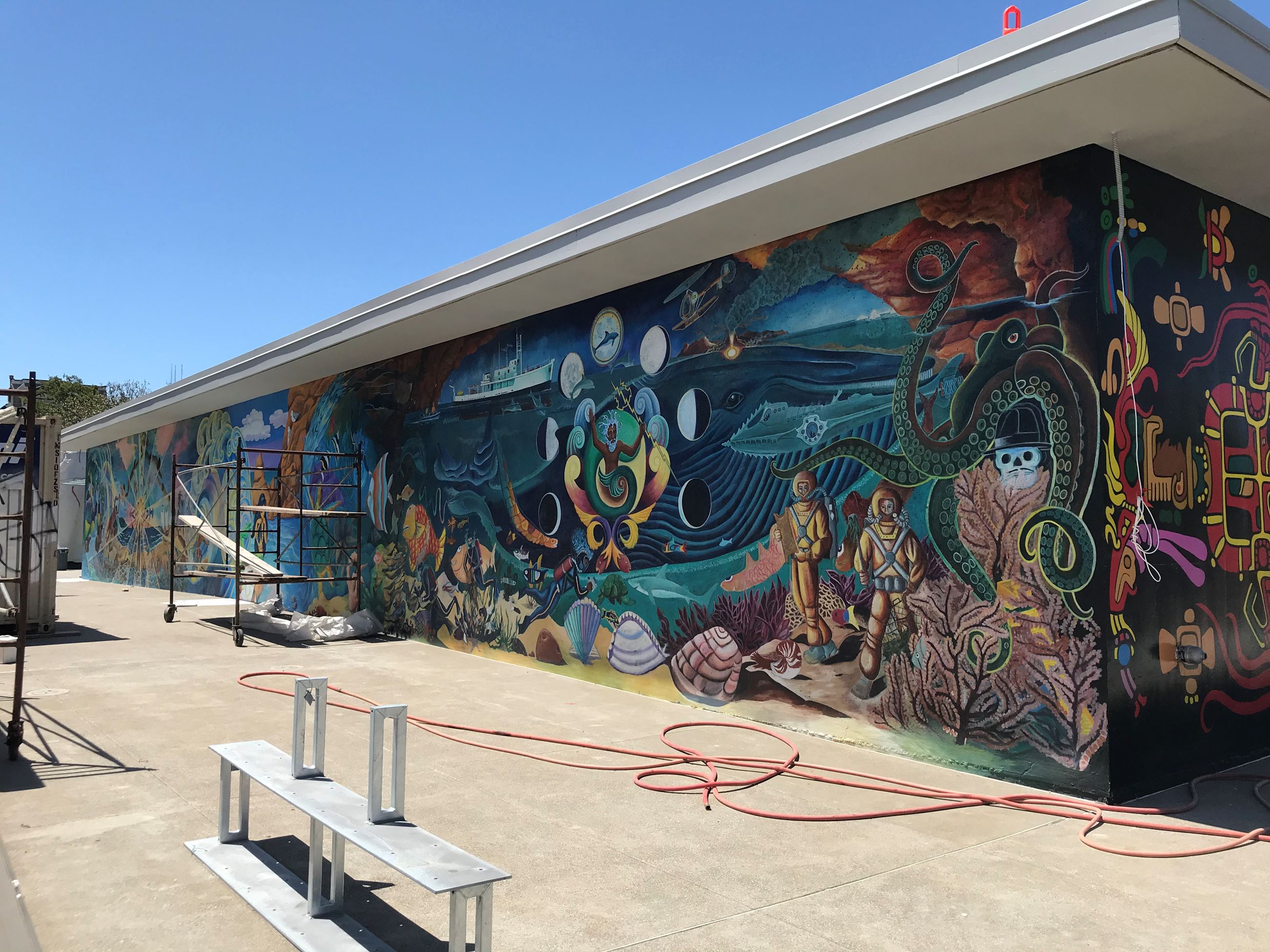 On the far left side of the mural is a green octopus underneath a red clay cliff, below is is two sc