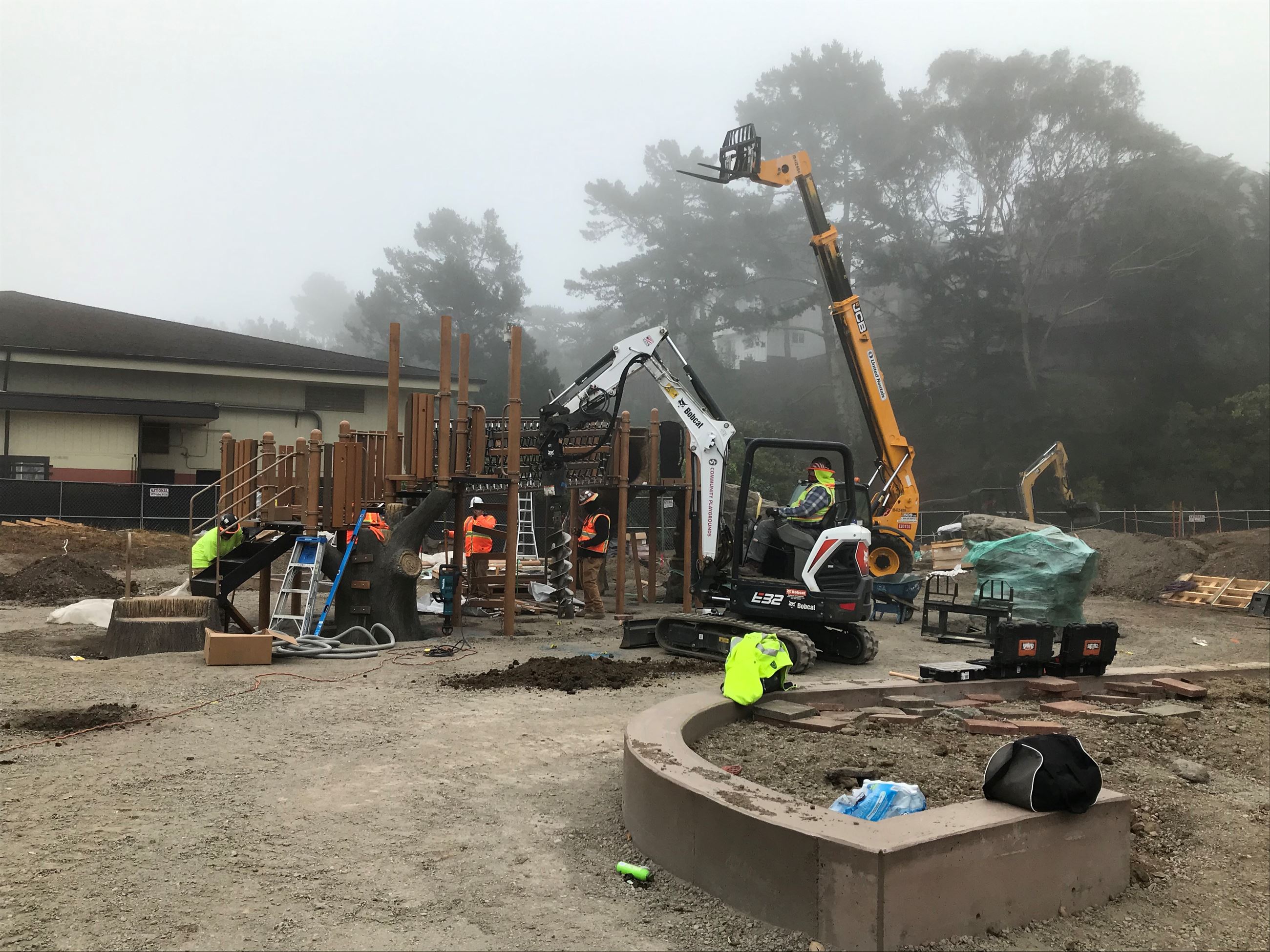 Small heavy equipment machines placing the playground structure featuring fabricated trees and wood