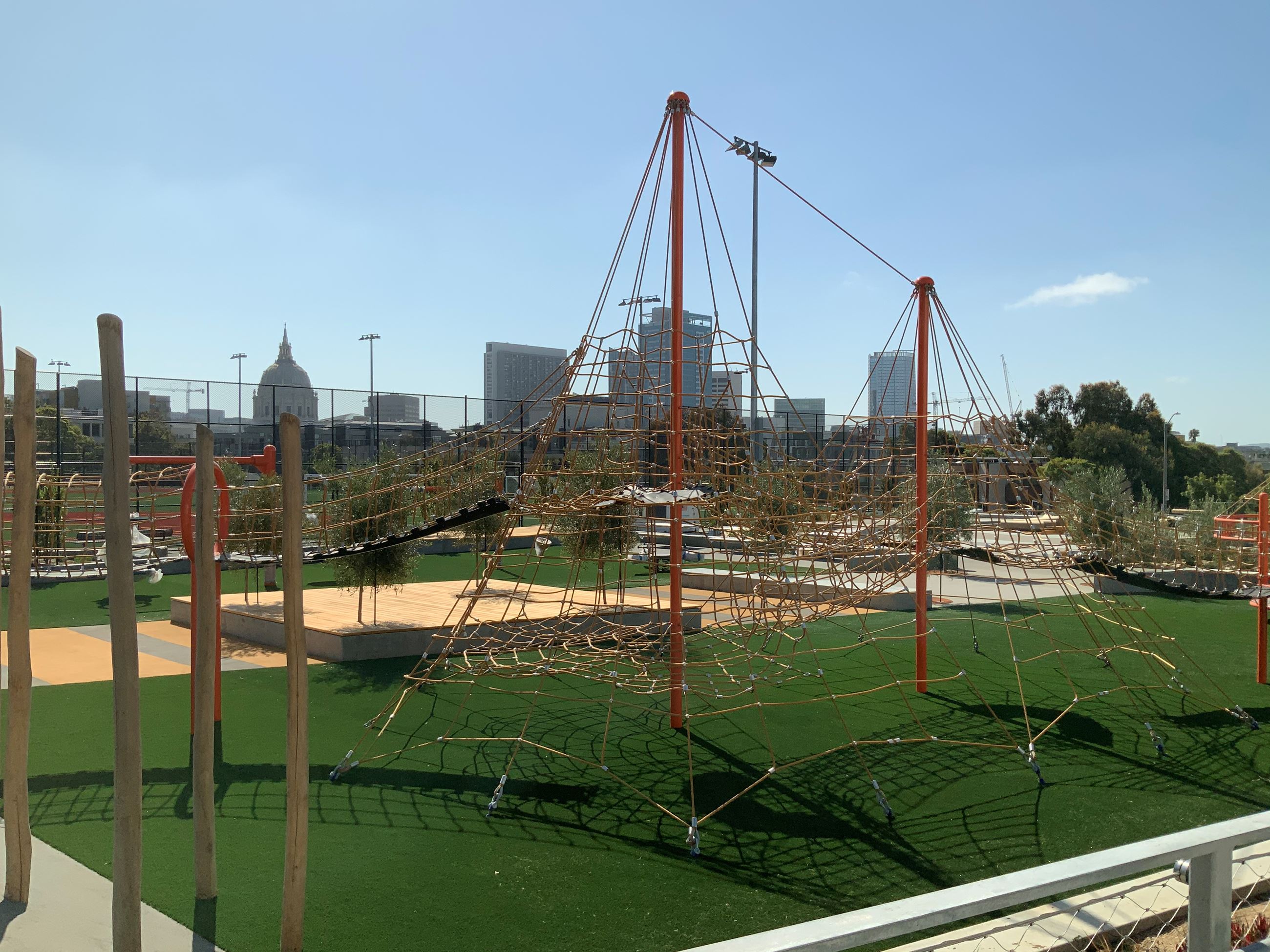 Climbing structure with climbing rope and orange poles, Cityscape in the background