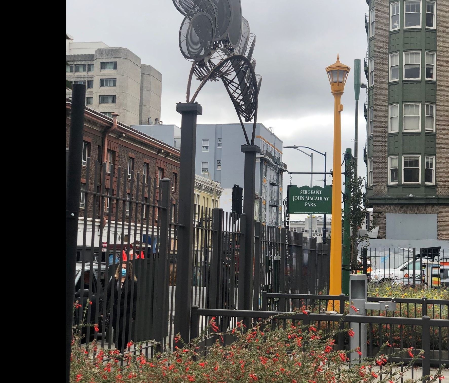metal sculpture over entry gate, black fences surrounding planter, yellow light pole