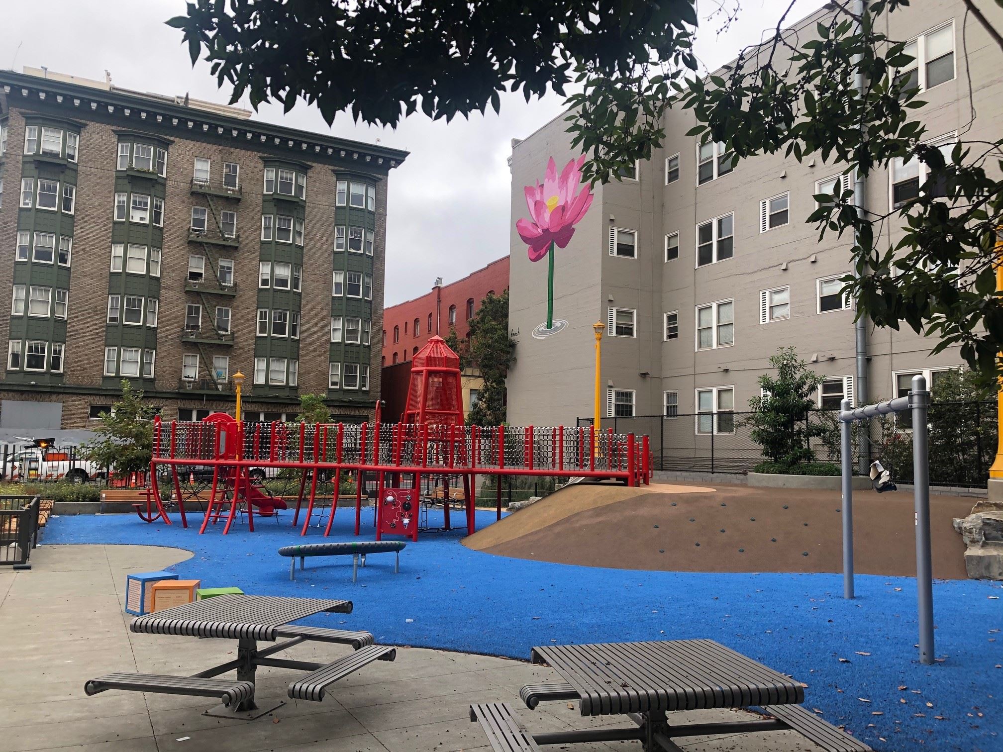 Red play structure, blue play surface, silver metal picnic tables, pink painted flower