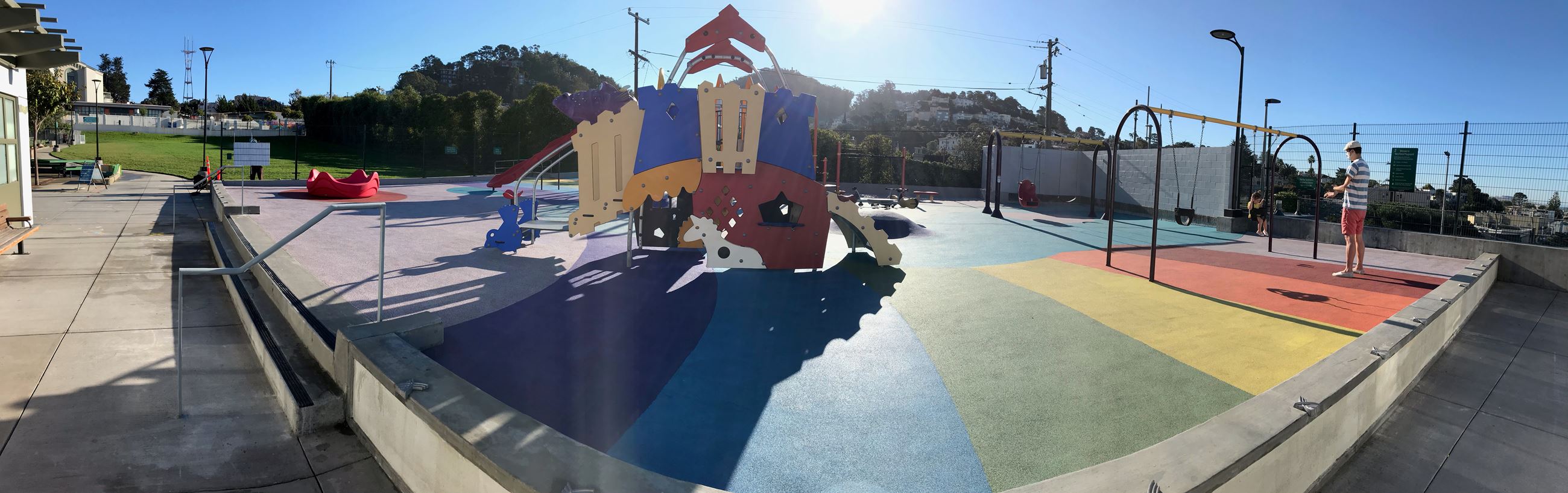 Play equipment, two sets of swings, rainbow colored safety surfacing on the ground