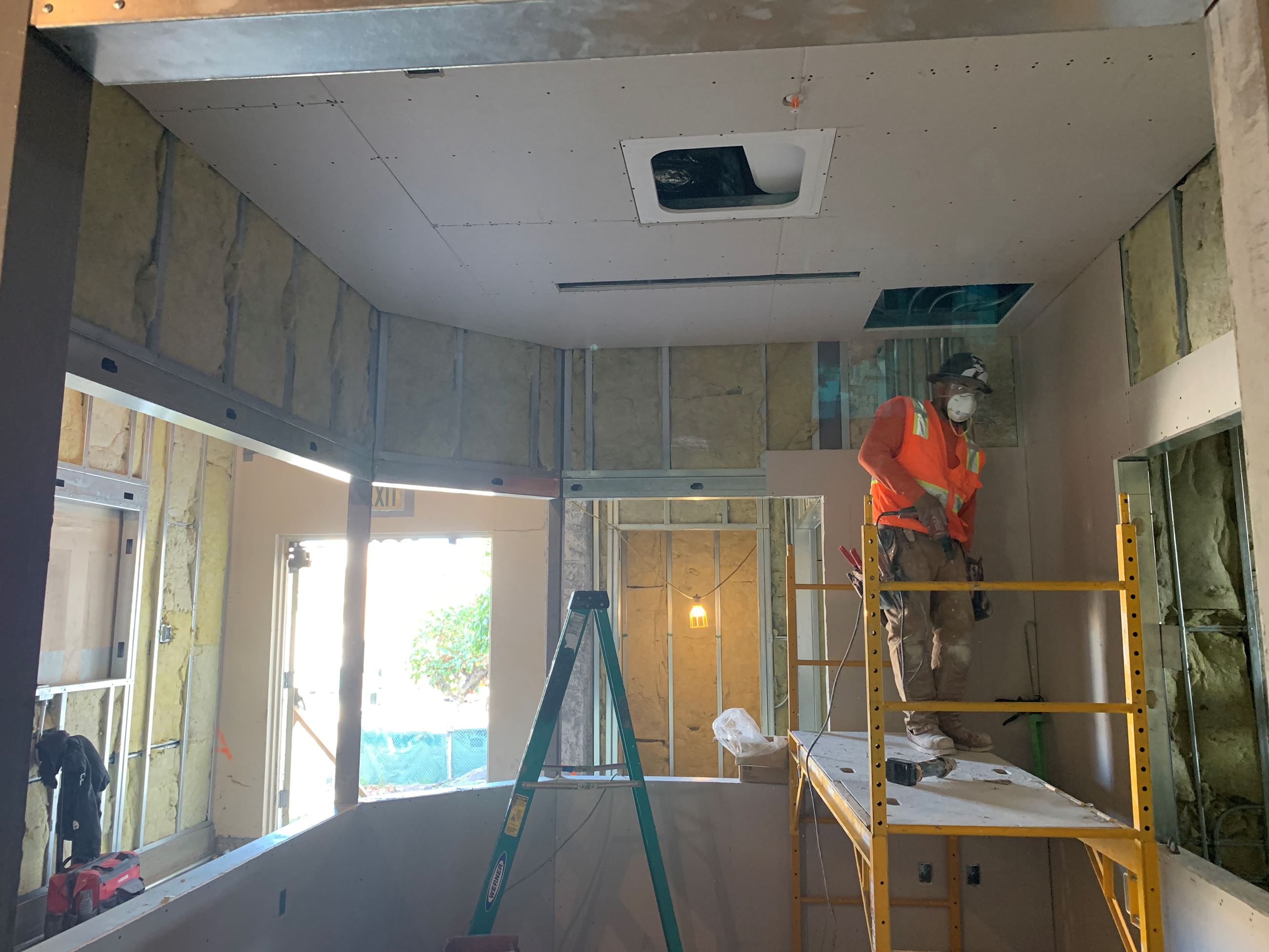Construction worker installing drywall in front office of pool building.