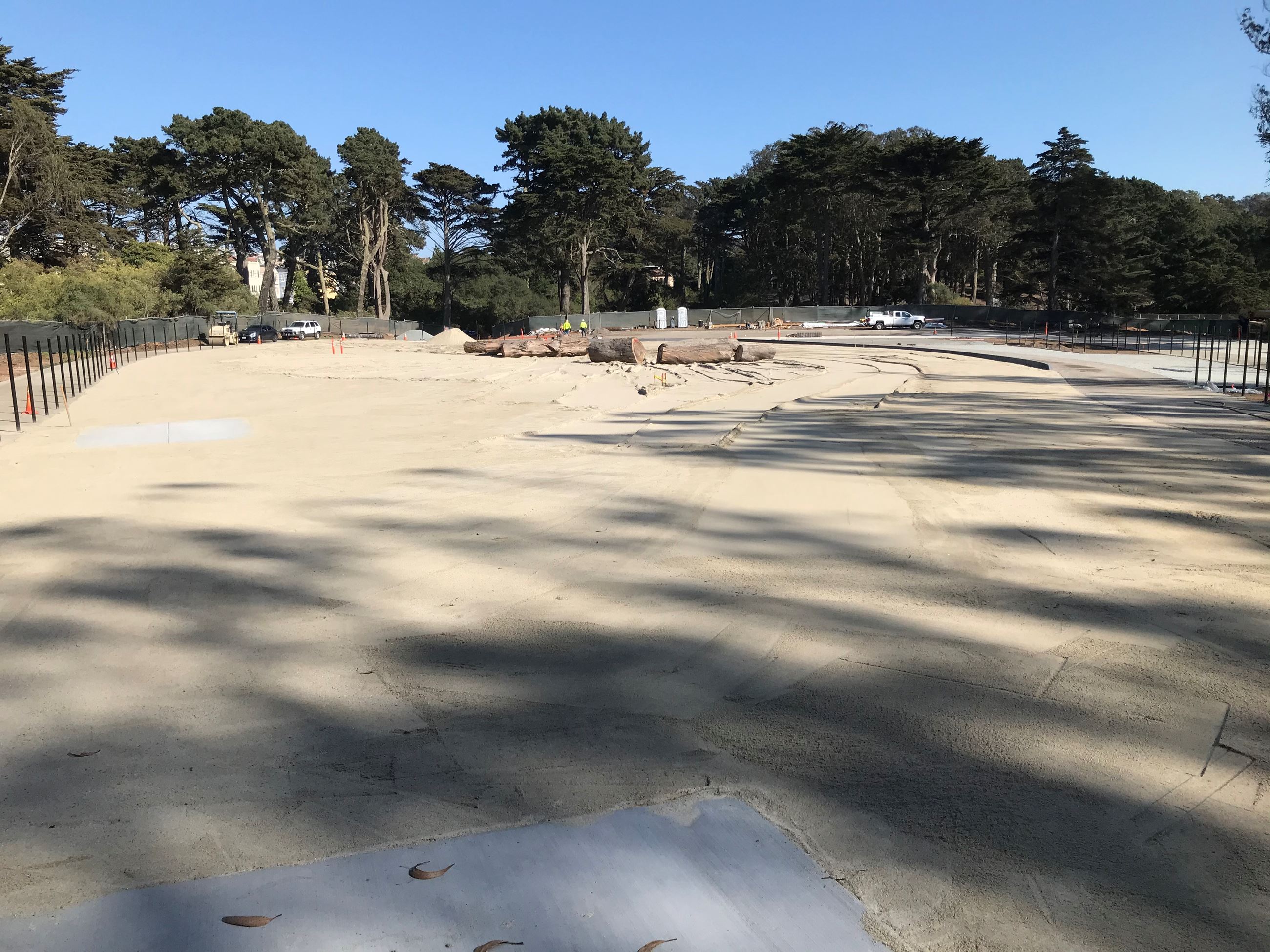 Two workers, four vehicles, black fence poles, freshly added sand and concrete curbing.