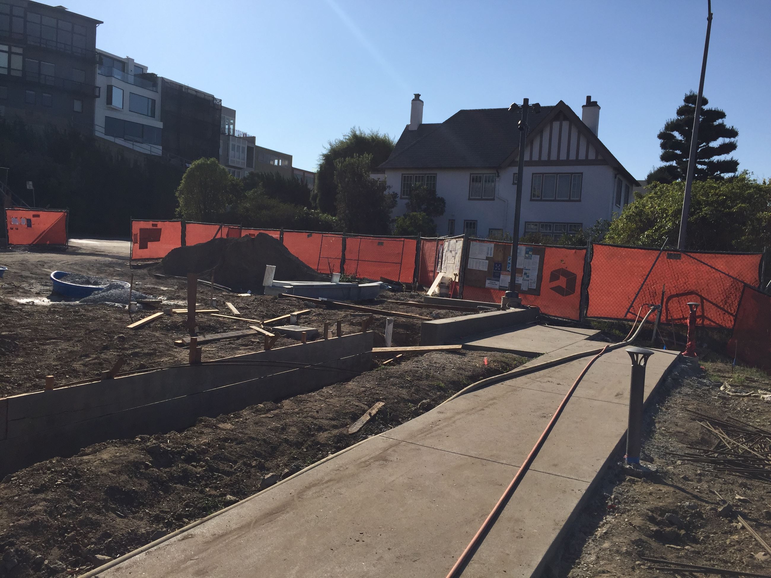 Garden bed wood structure, cement pathway with lighting, orange construction fence in background