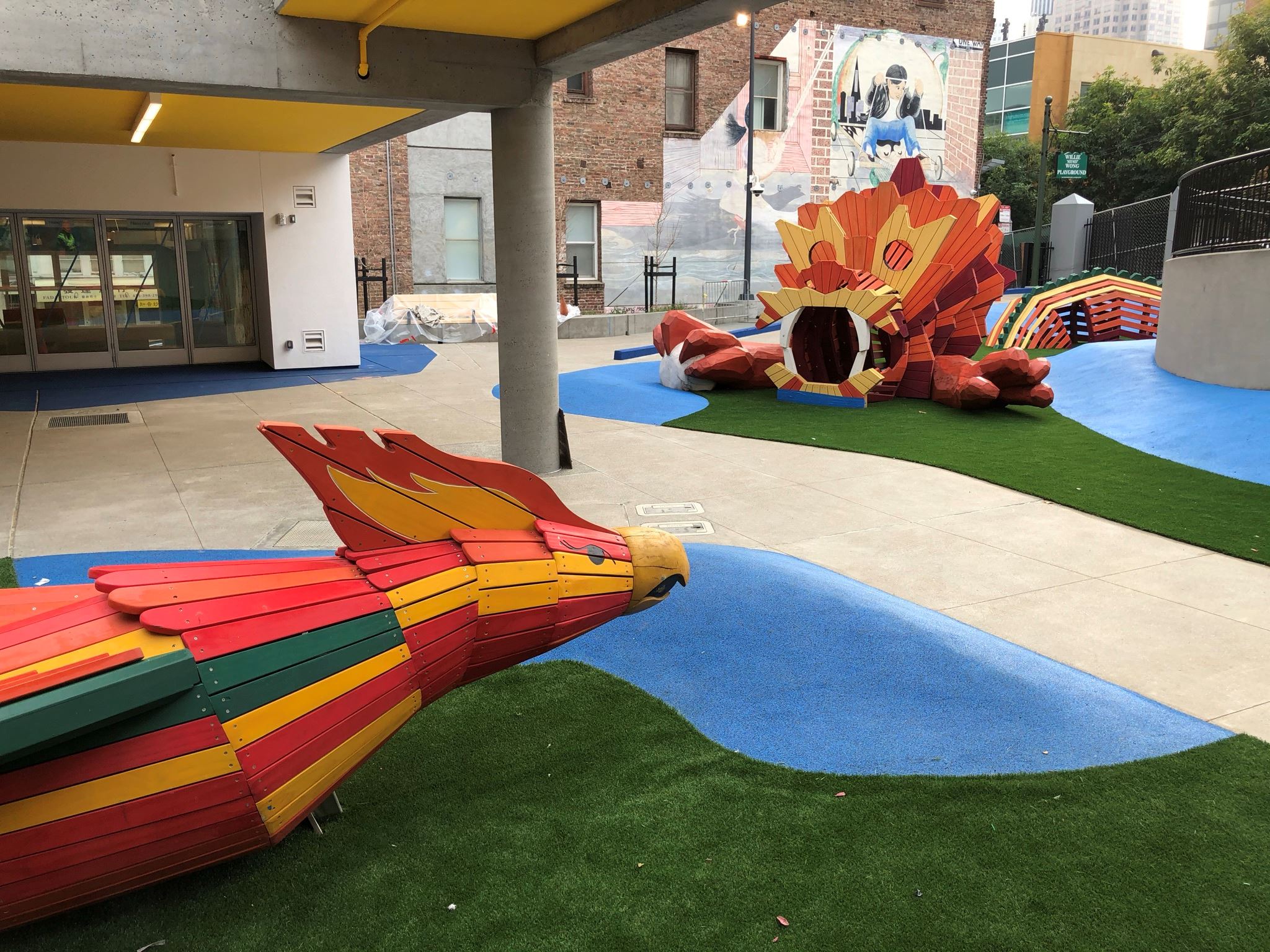 image shows two vibrant orange dragon play structures, green and blue safety surfacing