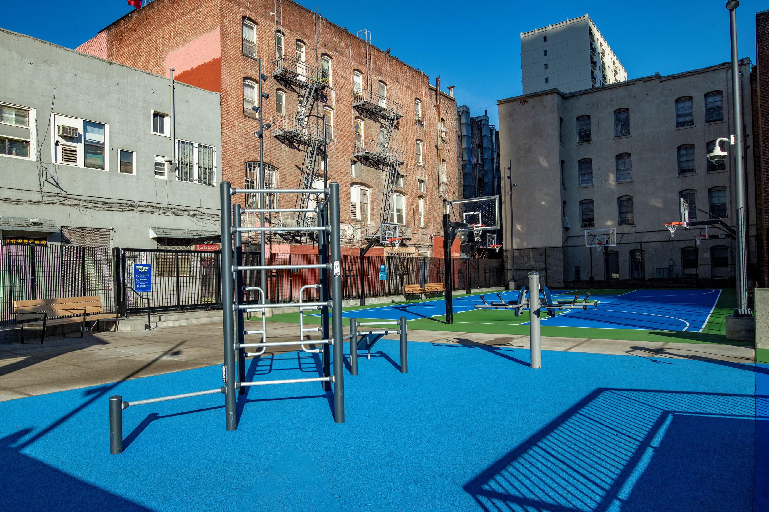 Adult fitness equipment over blue surface in the foreground and basketball courts in the background