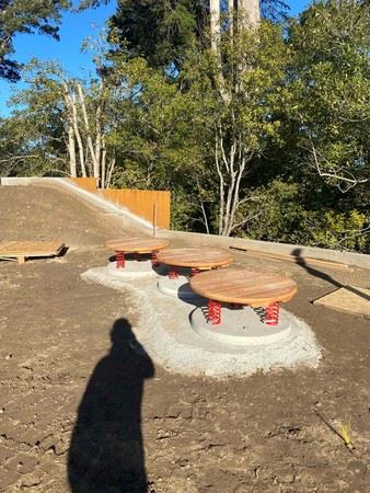 three Round play structures with wood tops and red springs underneath sitting on concrete pads