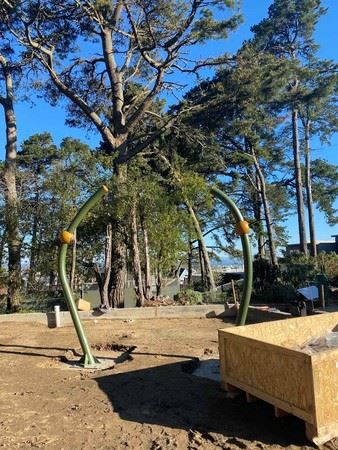 Two large green poles being installed to hold the saucer swing over unfinished soil.