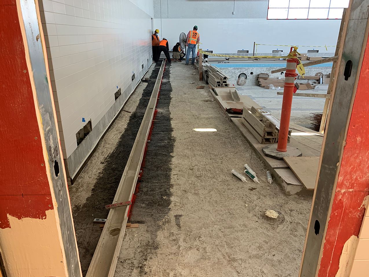 Three construction wokers in orange safety gear working on the pool deck.