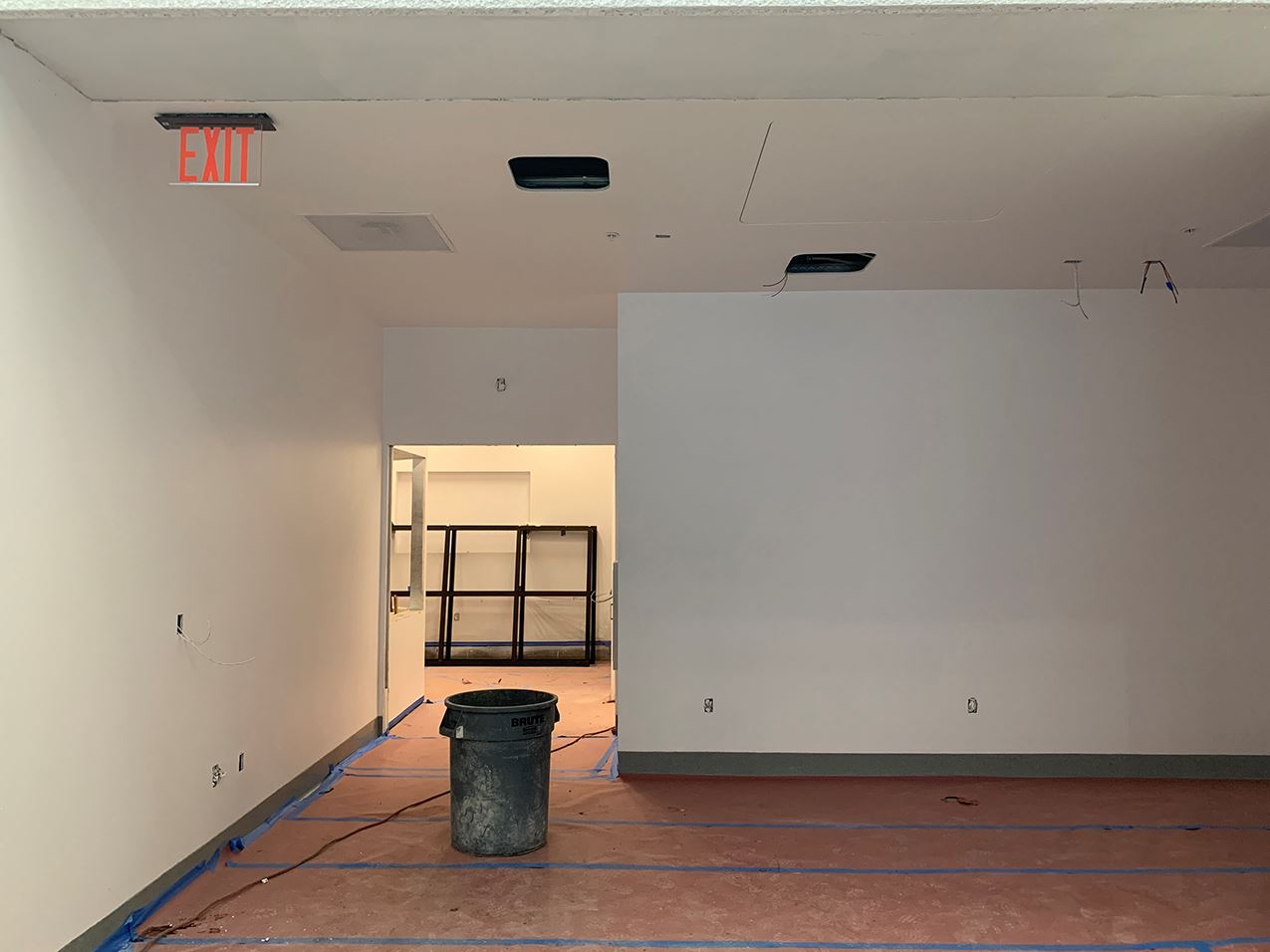 Interior room with white walls, floor covered in brown protective paper looking out at black shelves