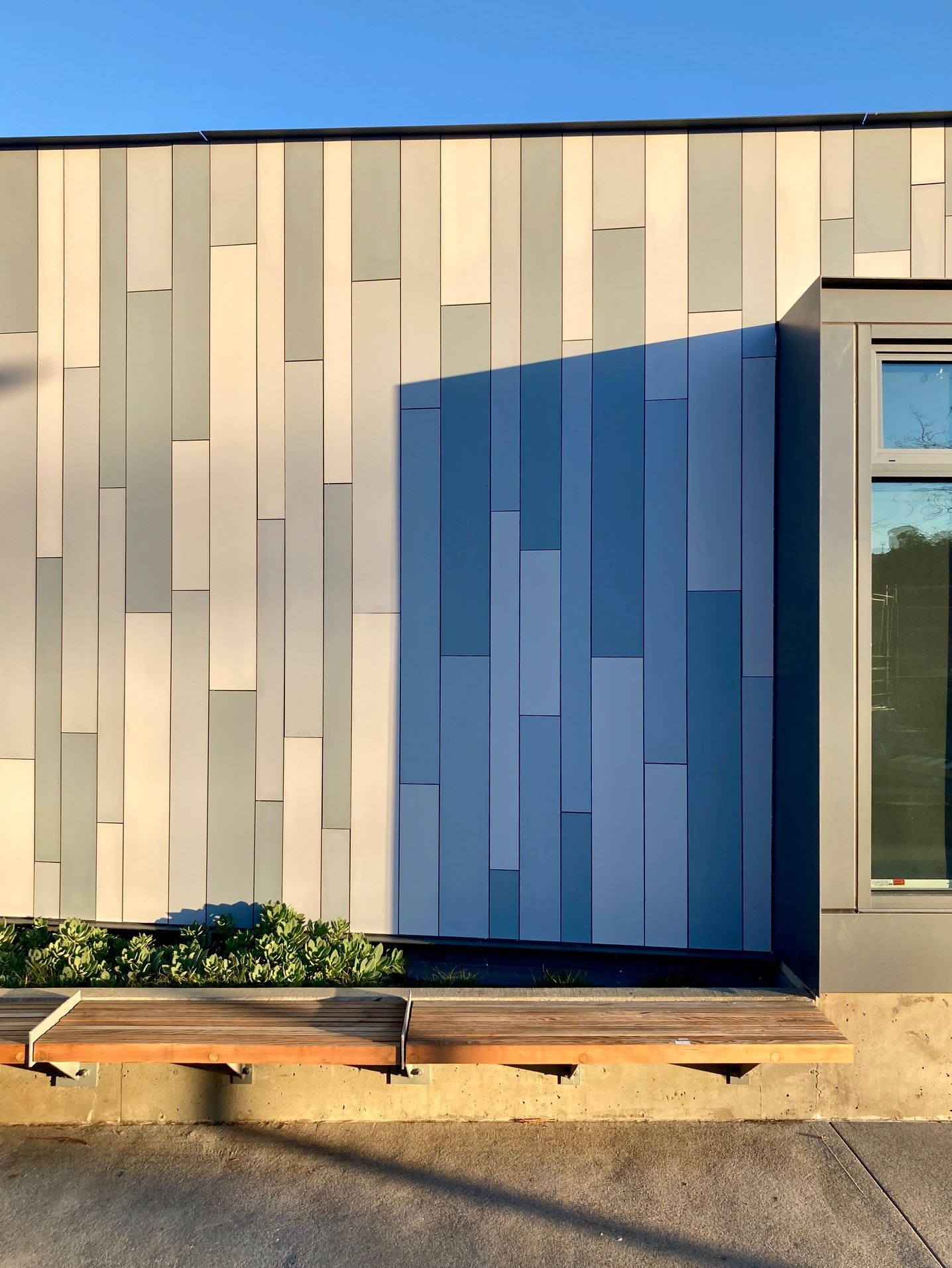 Exterior of the building, mixed grey color tiles, front door and wood bench.