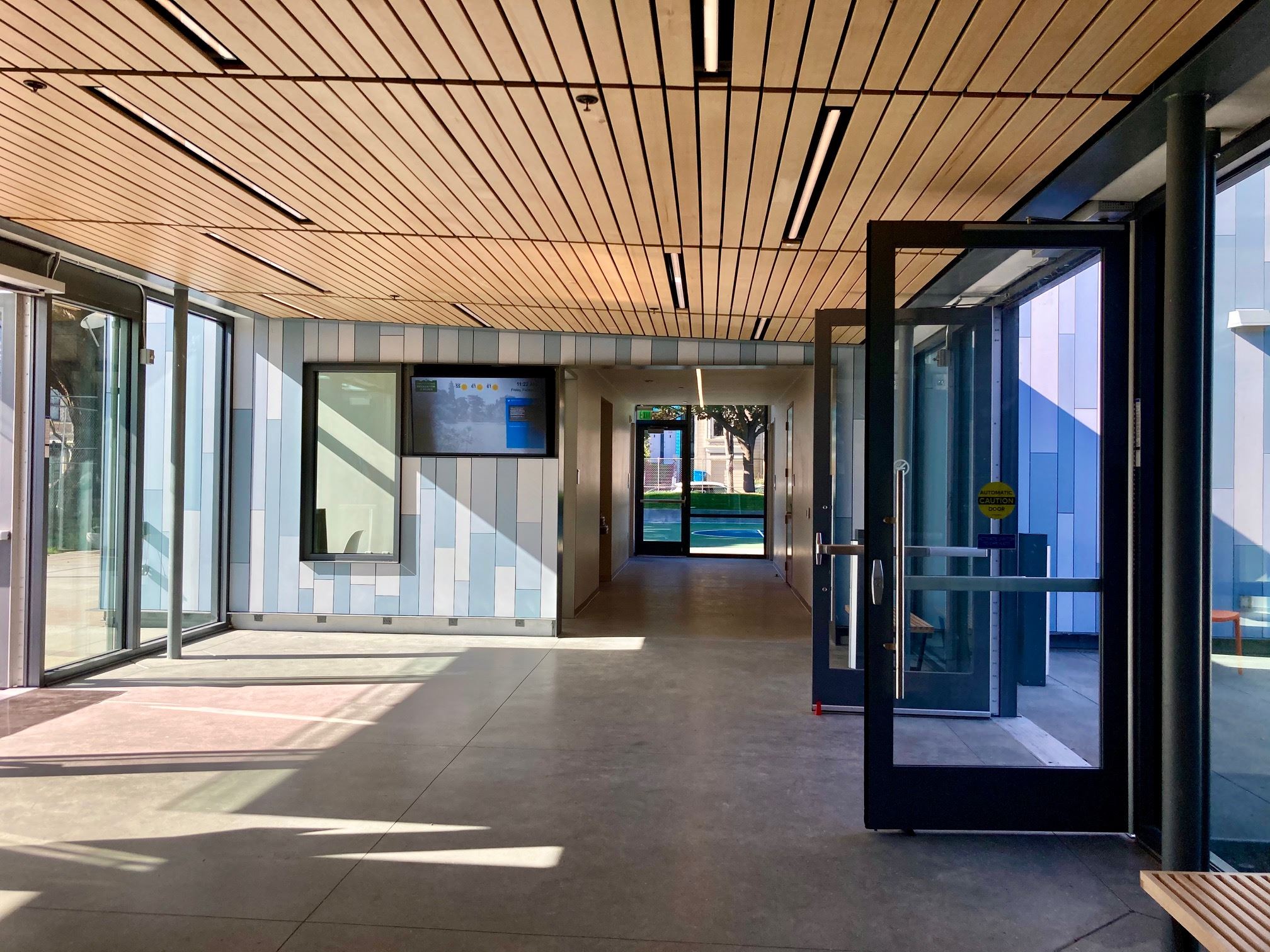 Interior foyer with large windows, multi shades of grey tile wall, and wood slat ceiling.