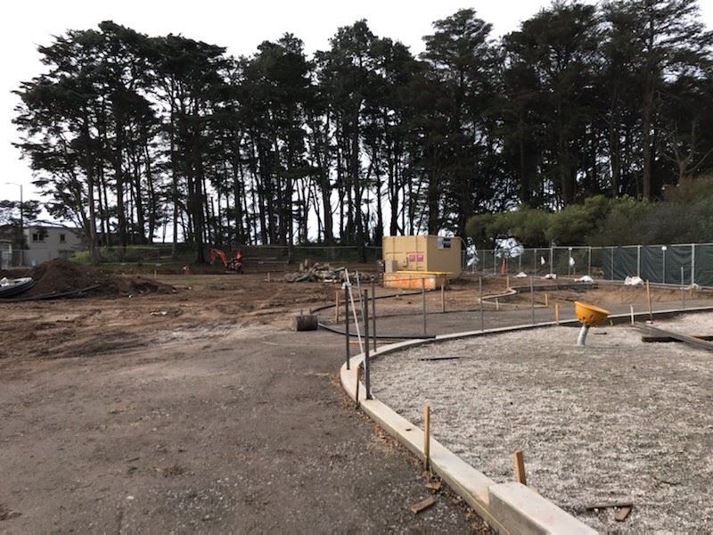 Large open dirt area with construction materials and large shipping container. Edge of playground.