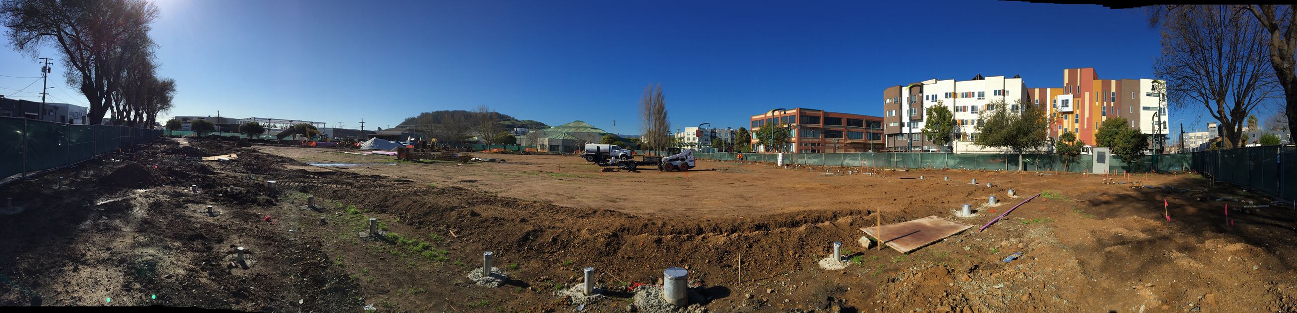 Fence post foundations seen in the foreground with heavy equipment and construction crews behind