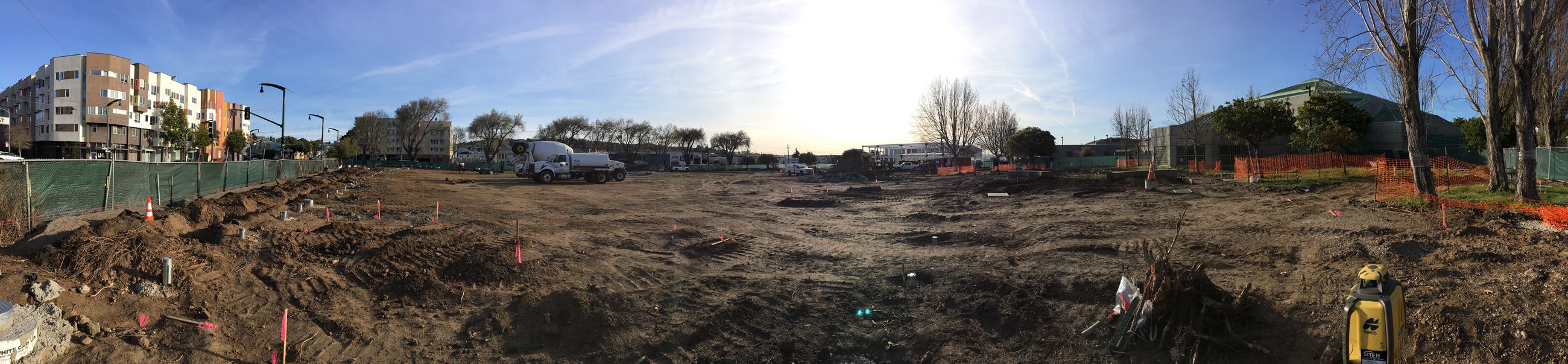 Dirt lot with heavy equipment and orange construction fencing.