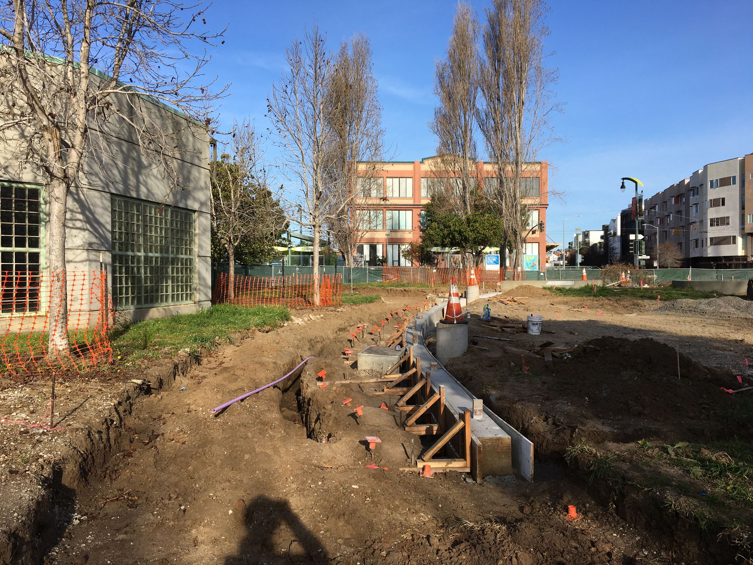 Playground fence foundation surrounded by soil and an orange construction fence.