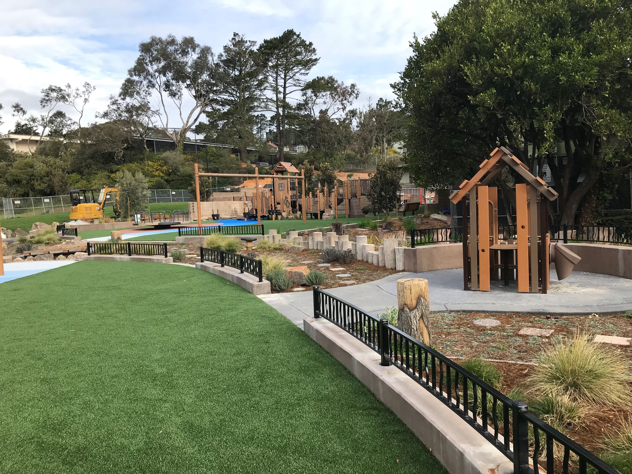 Wood play structure in the background with green safety surfacing short black metal fence dividers