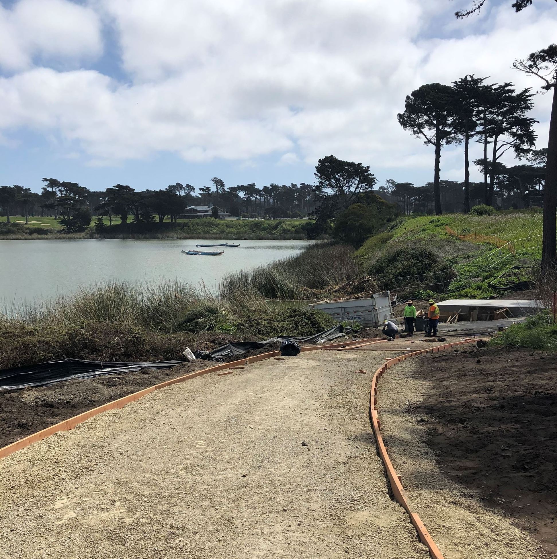 Two construction workers at the end of an unfinished pathway next to the lake.