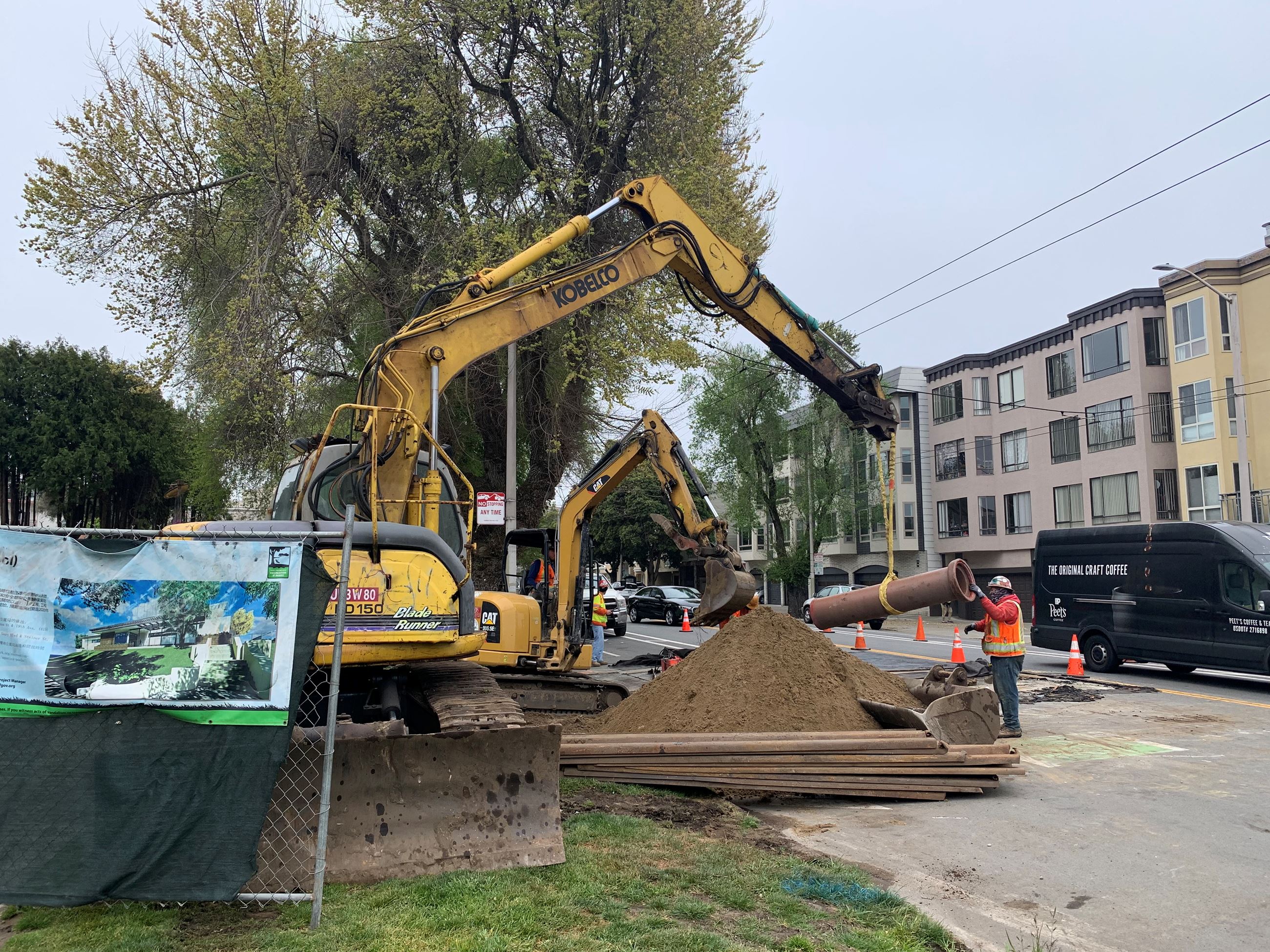 Three construction workers operating two yellow excavators installing pipe to the street.
