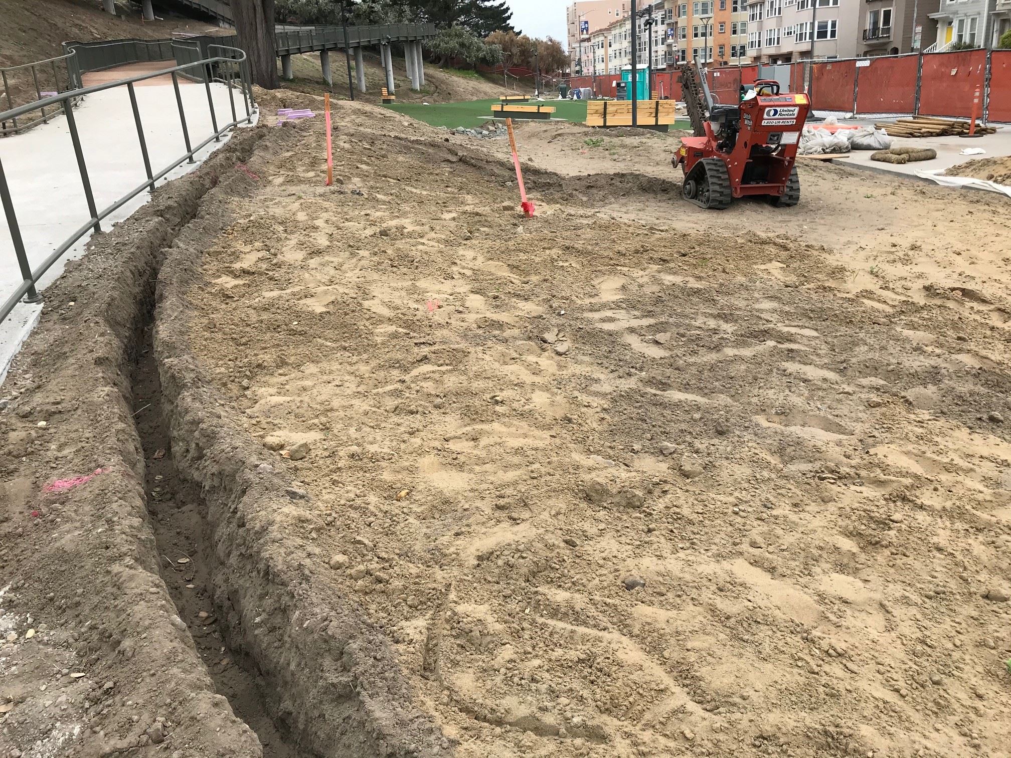 Cement pathway with green metal handrails to the left of exposed soil and dog area.
