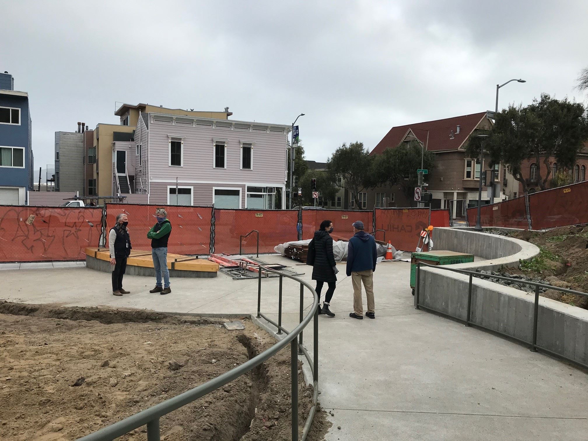 Four people standing at the end of the concrete pathway in front of a red mesh fence,