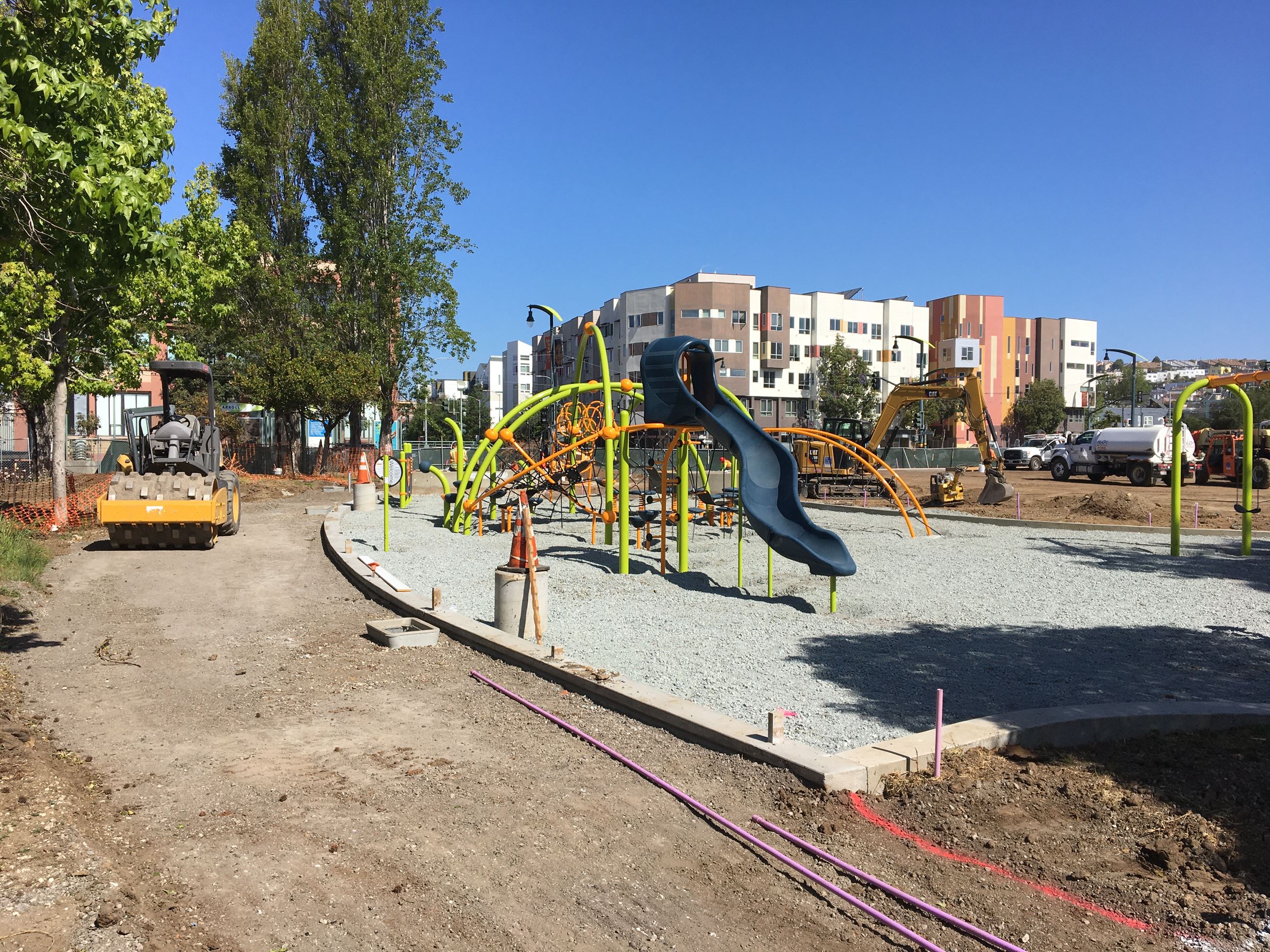 Playground equipment with slide. Cement curb with gravel rock underlayment and heavy equipment.