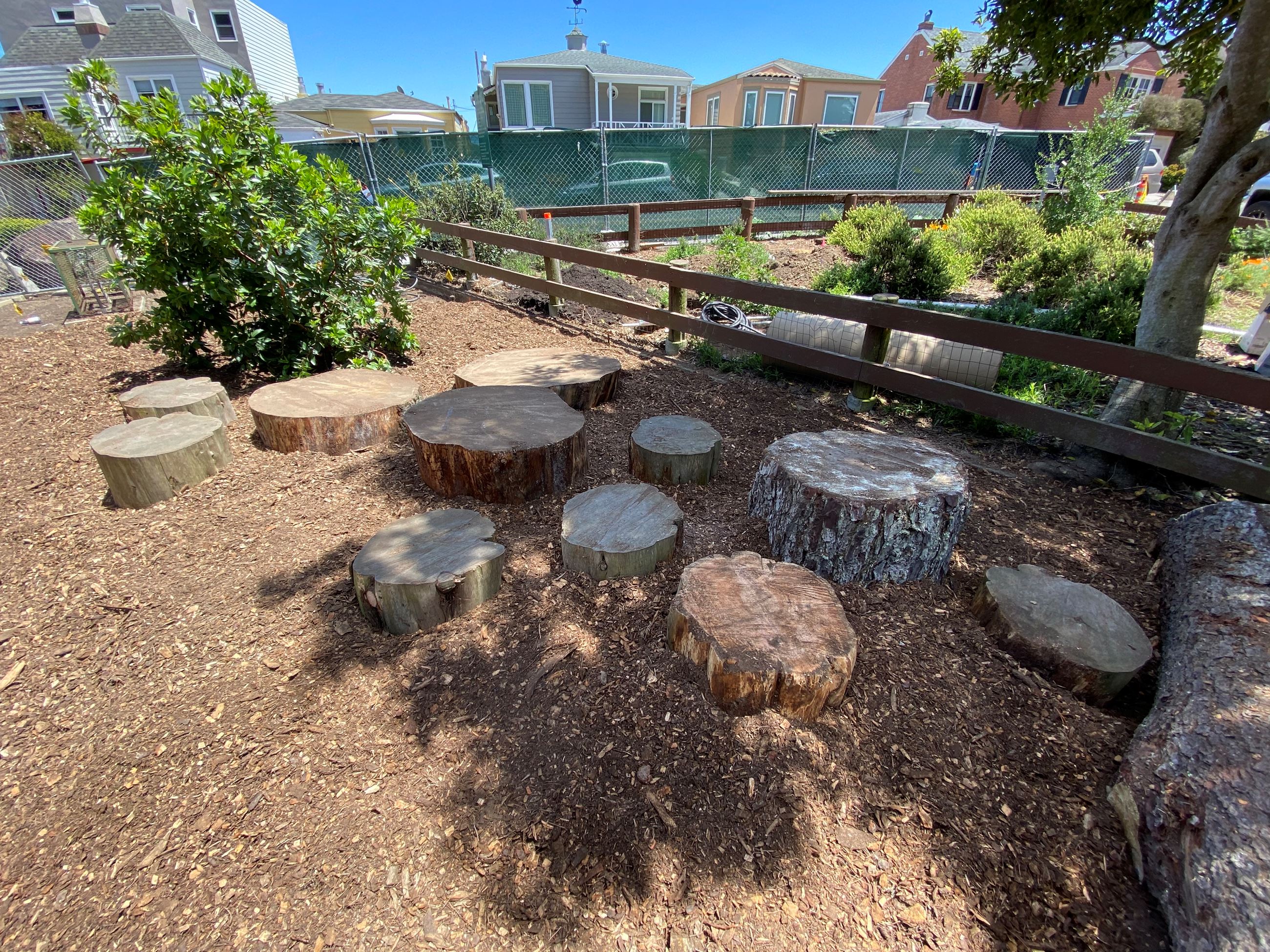 Nature play area with cut round log ends on top of wood chips, next to slat wood fence.