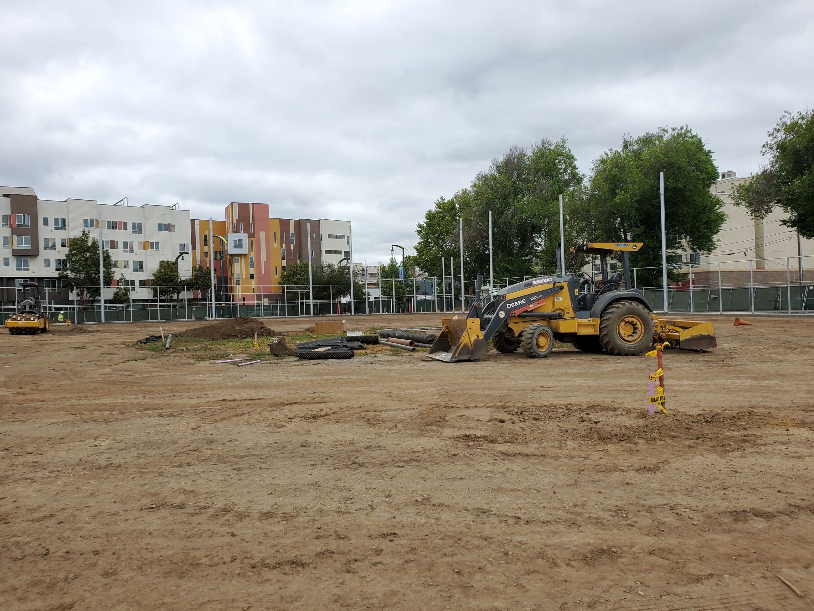 Ballfield backstop in the background, heavy equipment and exposed soil ballfield.