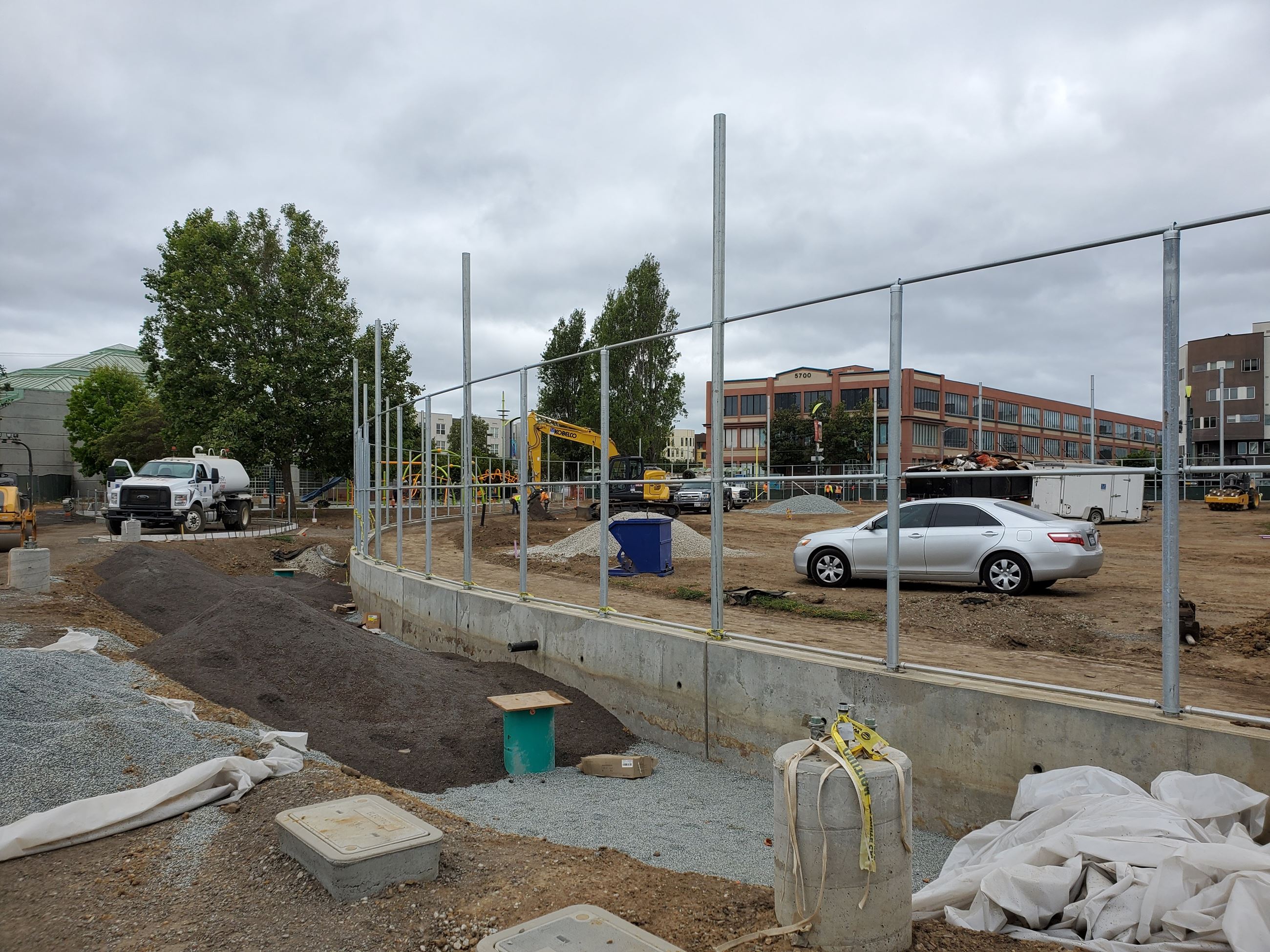 Heavy equipment, exposed soil for future bioswale. Cement foundation with metal fence skeleton.