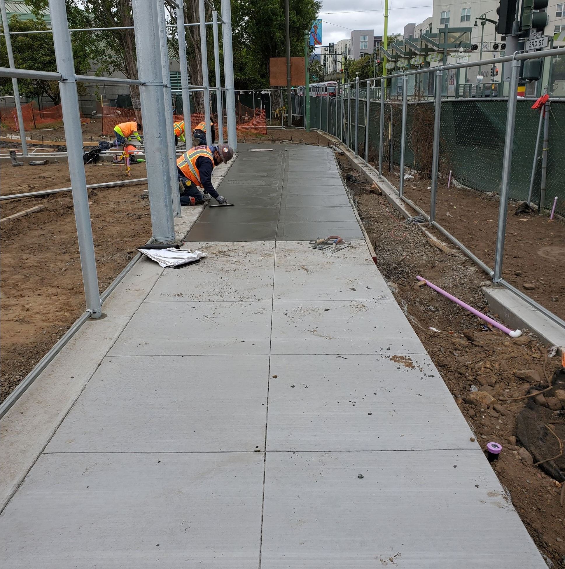 Four construction workers finishing the cement sidewalk along the ballfield.