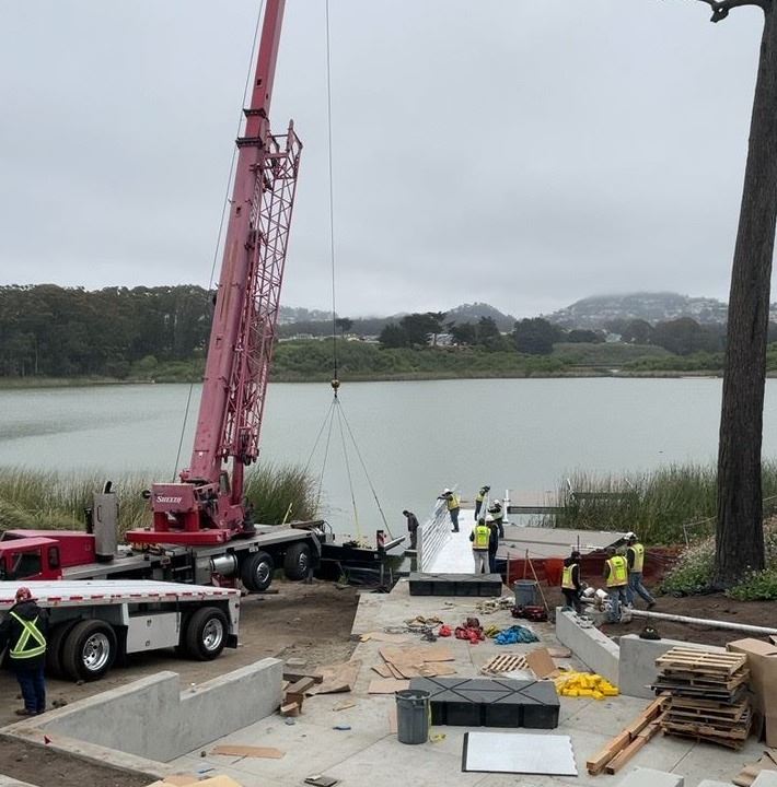 Large red crane moving materials with construction workers assisting.