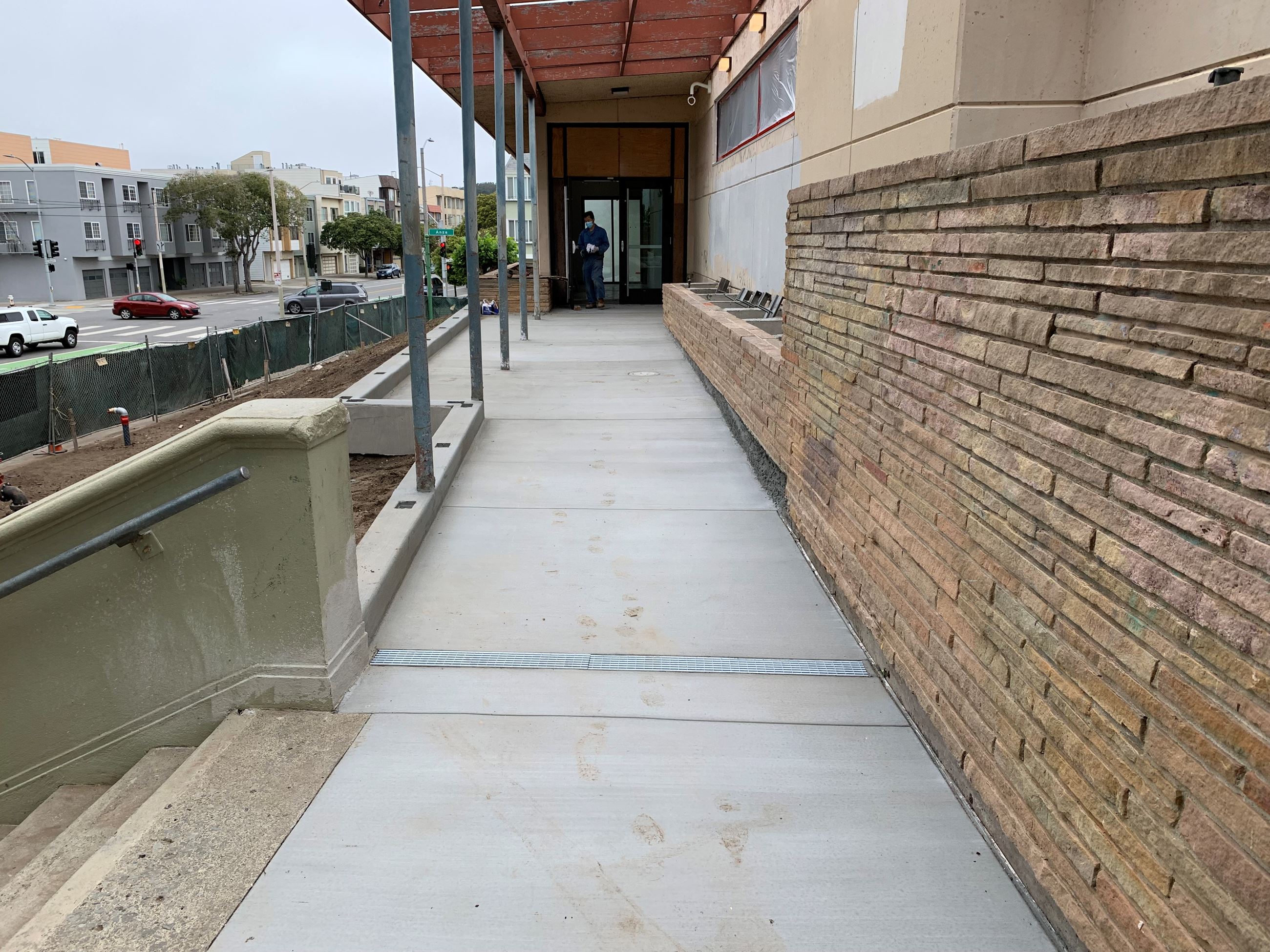 Concrete sidewalk poured in front of building entrance. Lower brick façade and wall of building.