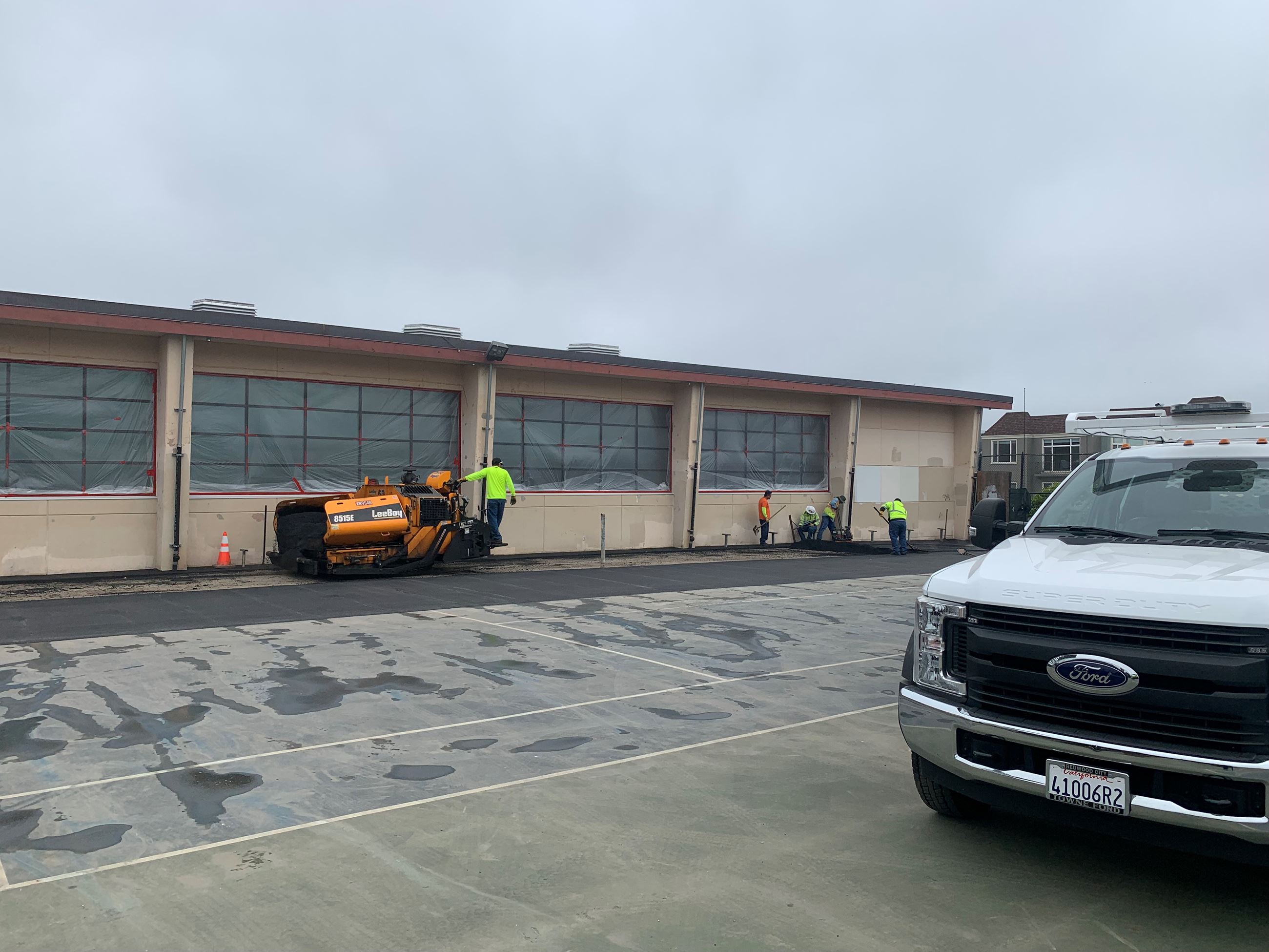 Exterior of pool building with plastic covering all of the windows and equipment adding concrete.