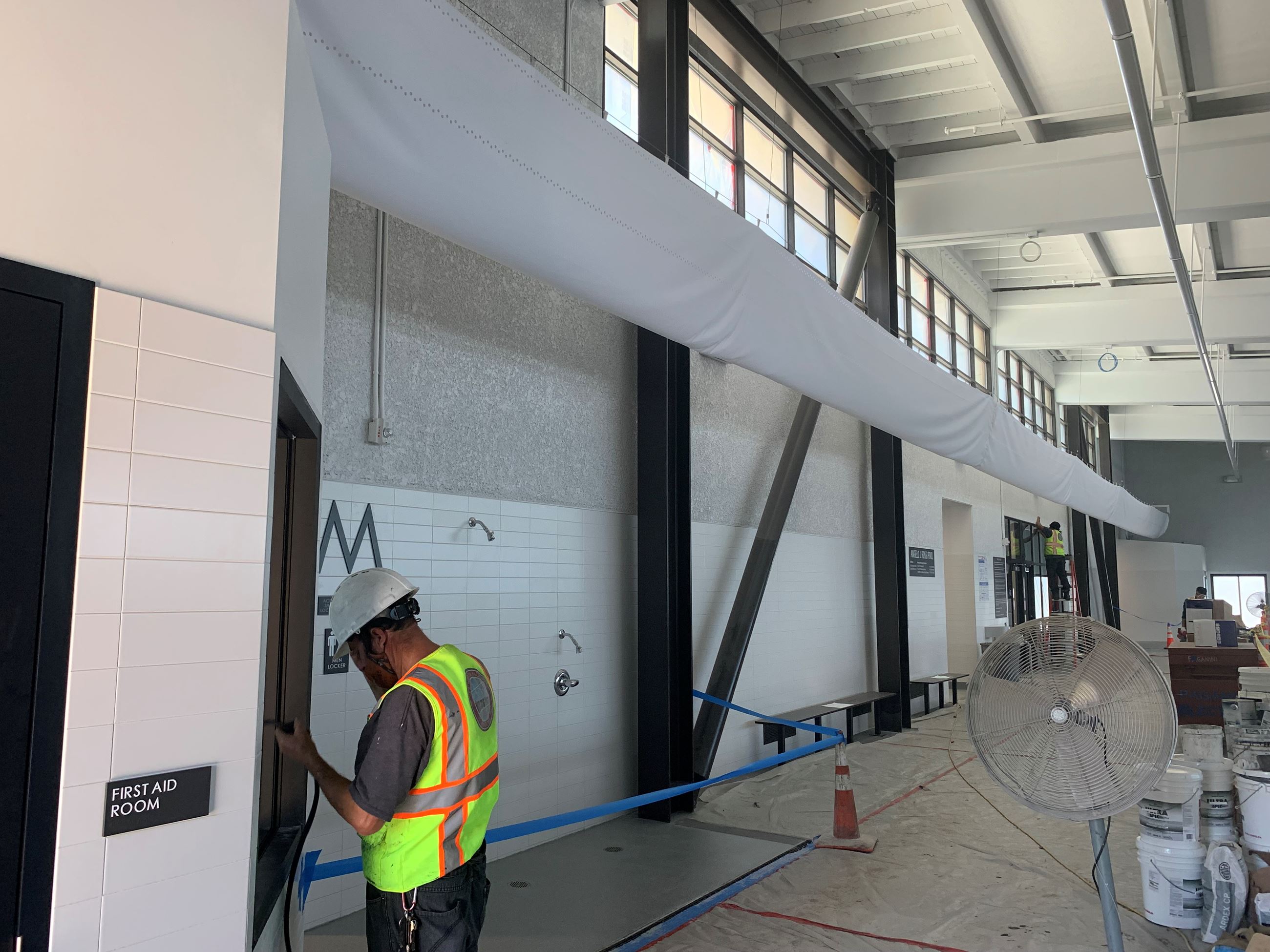 Construction workers finishing interior pool building. Two showers, white tile wall and black beams.
