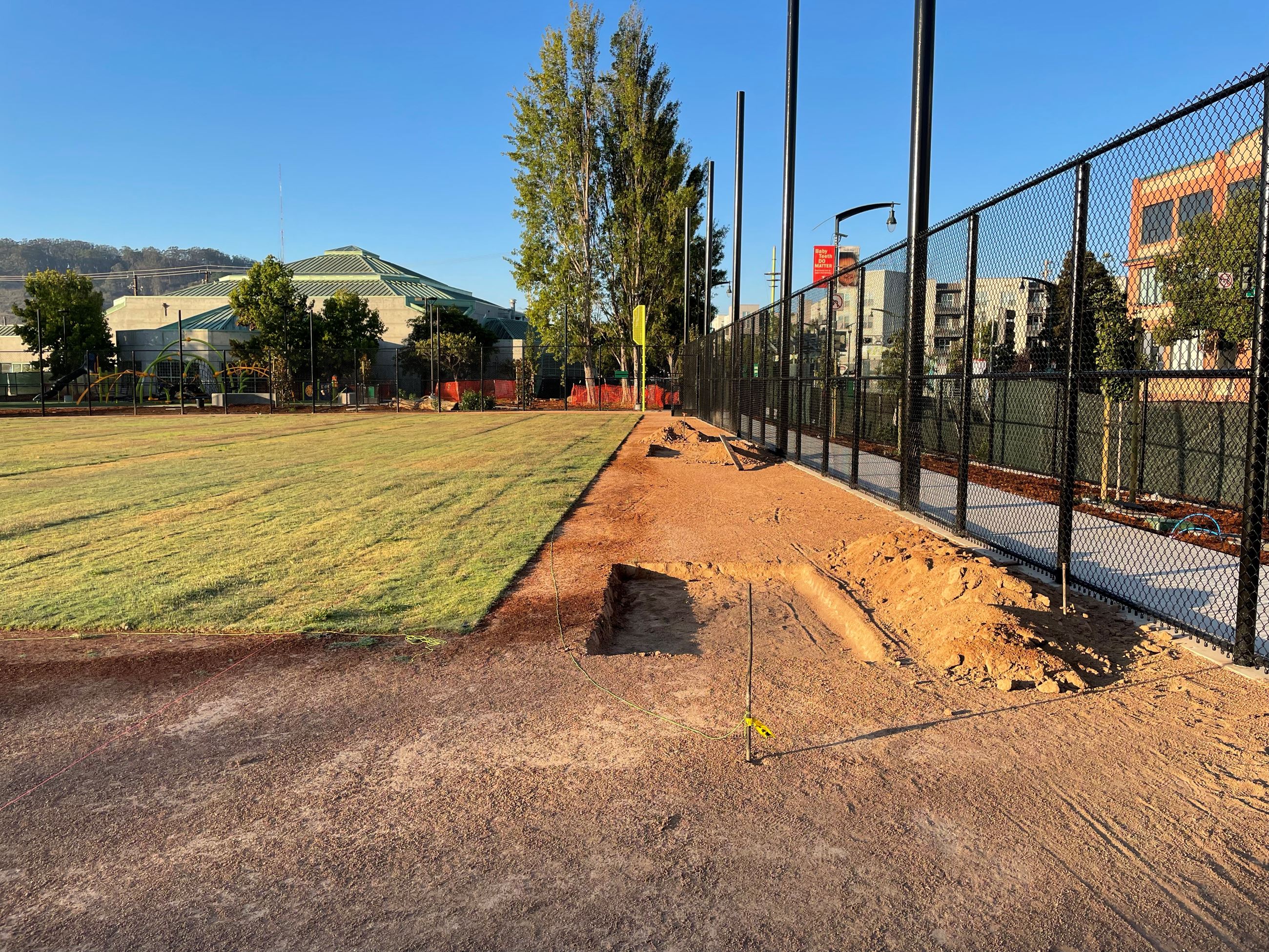Square holes dug in the dirt next to the new black chain link fence and sod