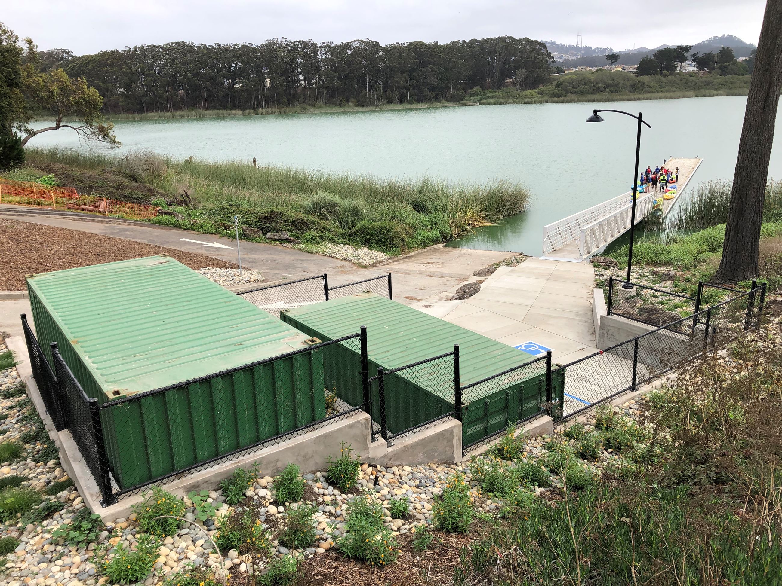 Two green shipping container sit next to an accessible parking space at the top of the boat dock