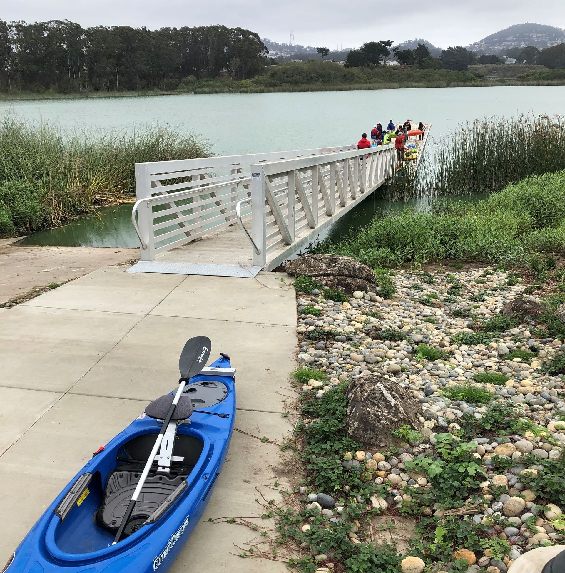 A blue kayak on the cement pad at the top of the boat dock in the foreground and people in the back