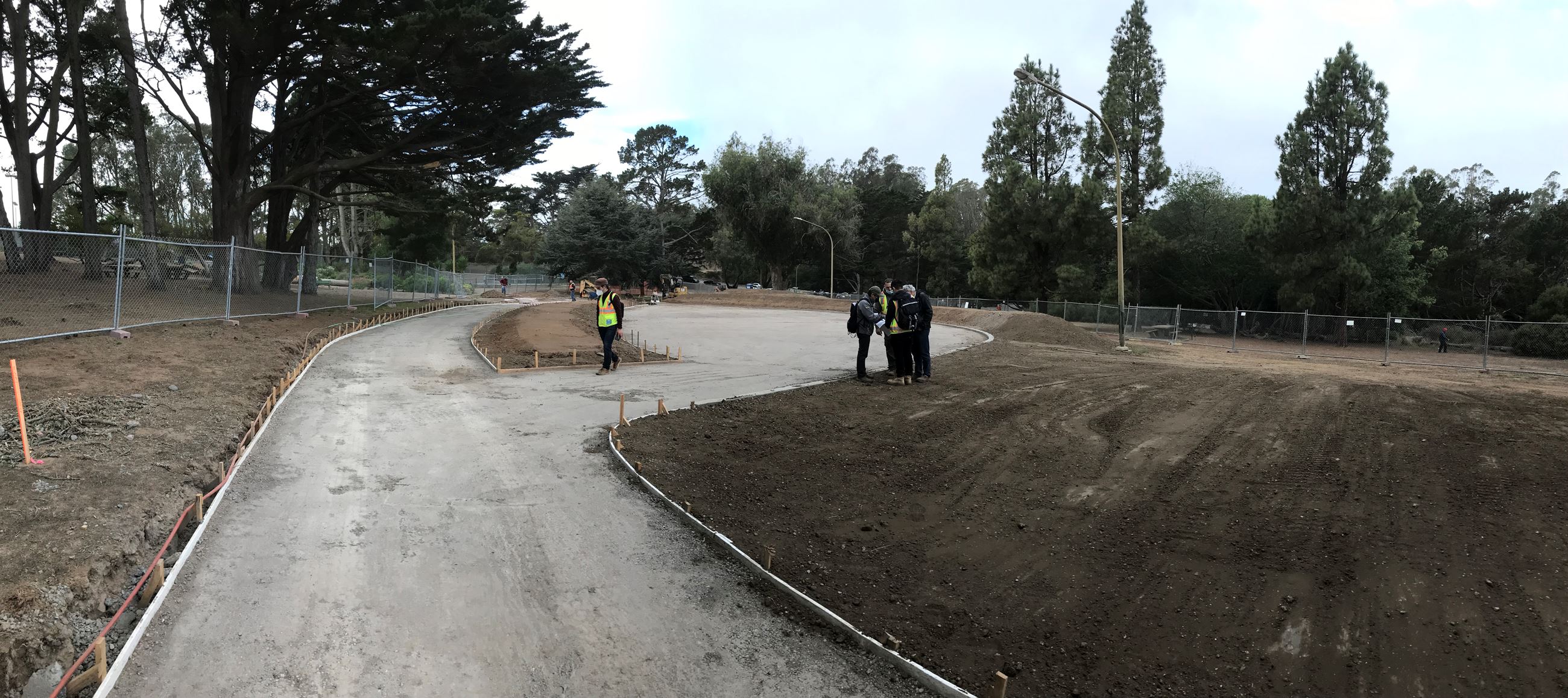 A group of people standing in the middle of graded area with heavy equipment in the background