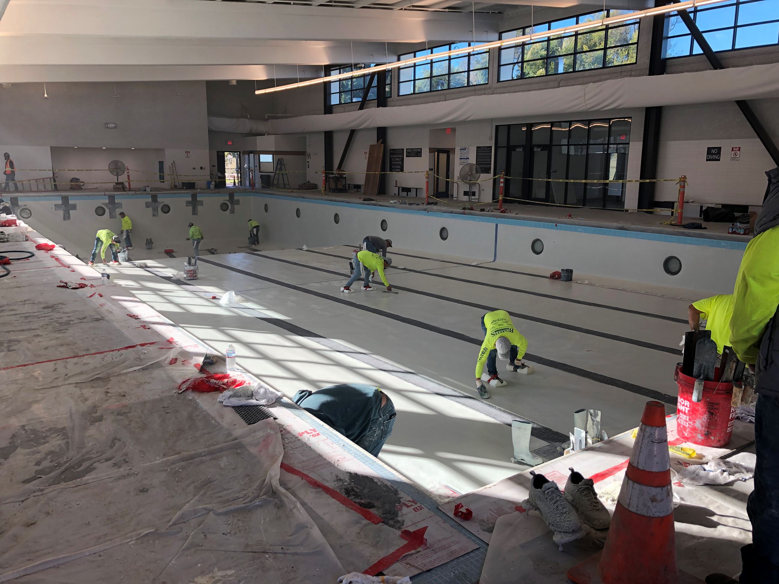 Seven construction workers wearing bright yellow shirts seen putting the last coating on the pool