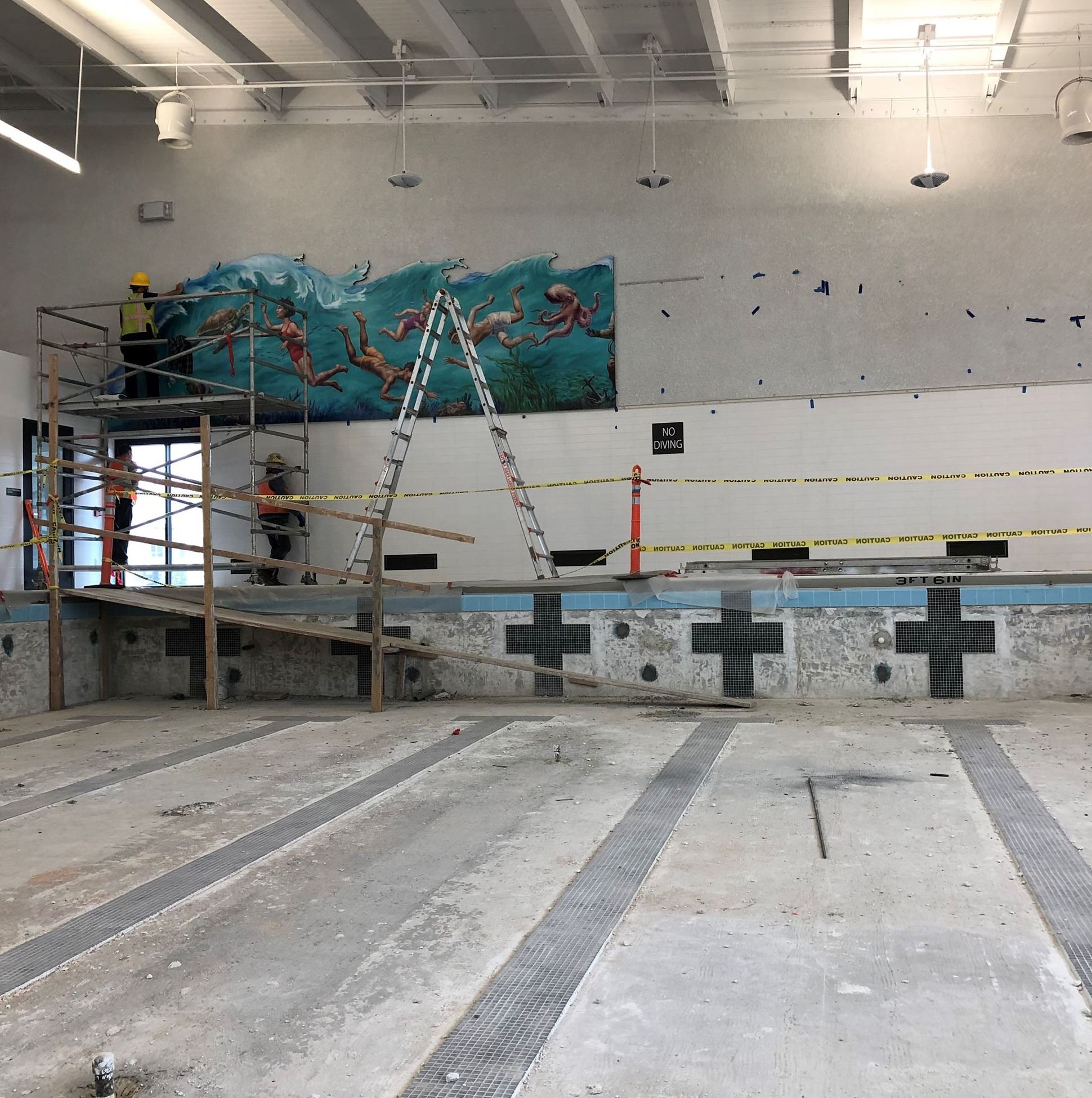 A large wall mural with ocean water and people swimming being painted on the back left corner wall.